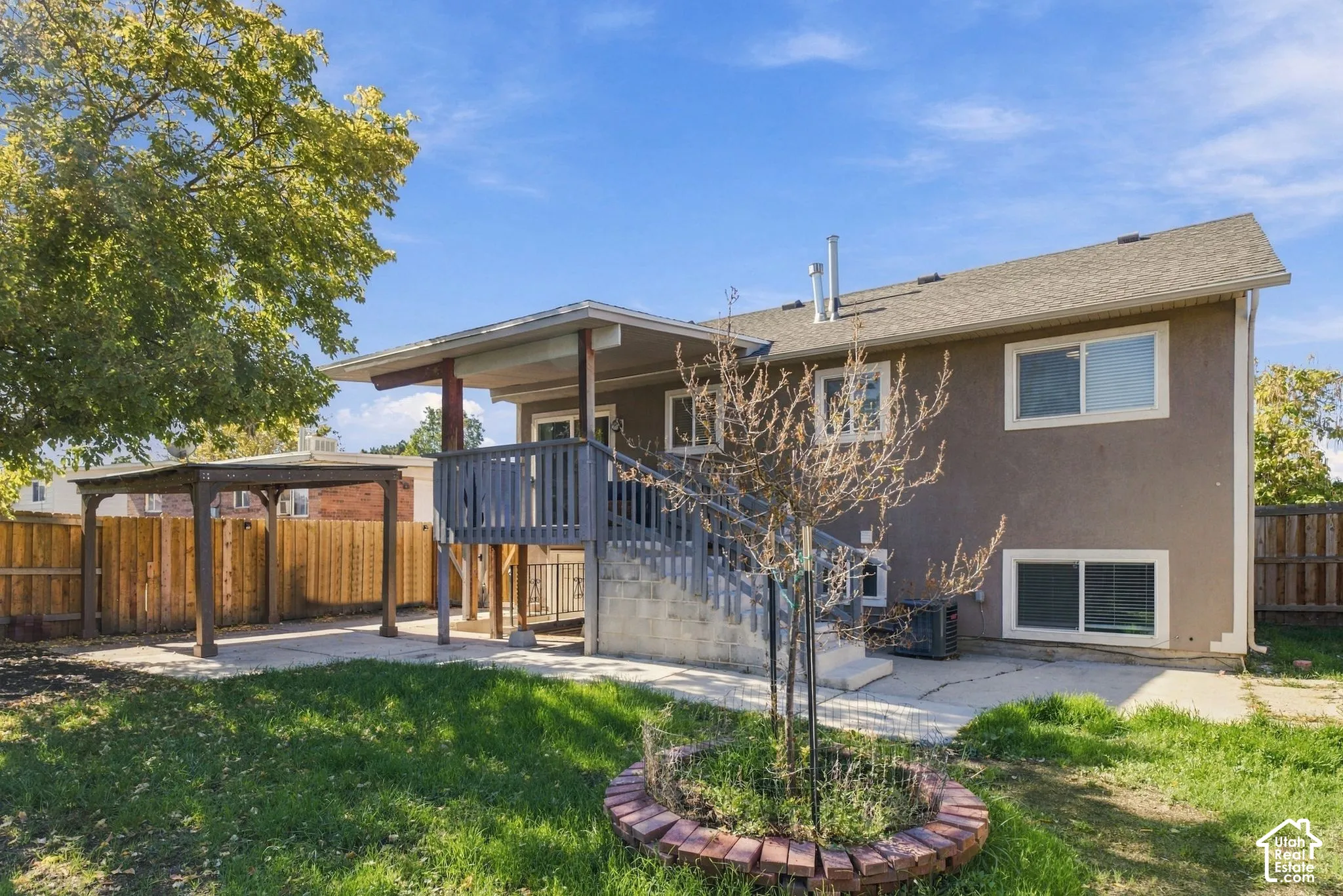 Backyard featuring an elevated wood deck, covered patio, concrete hardscaping, wood privacy fencing, and a circular brick planter