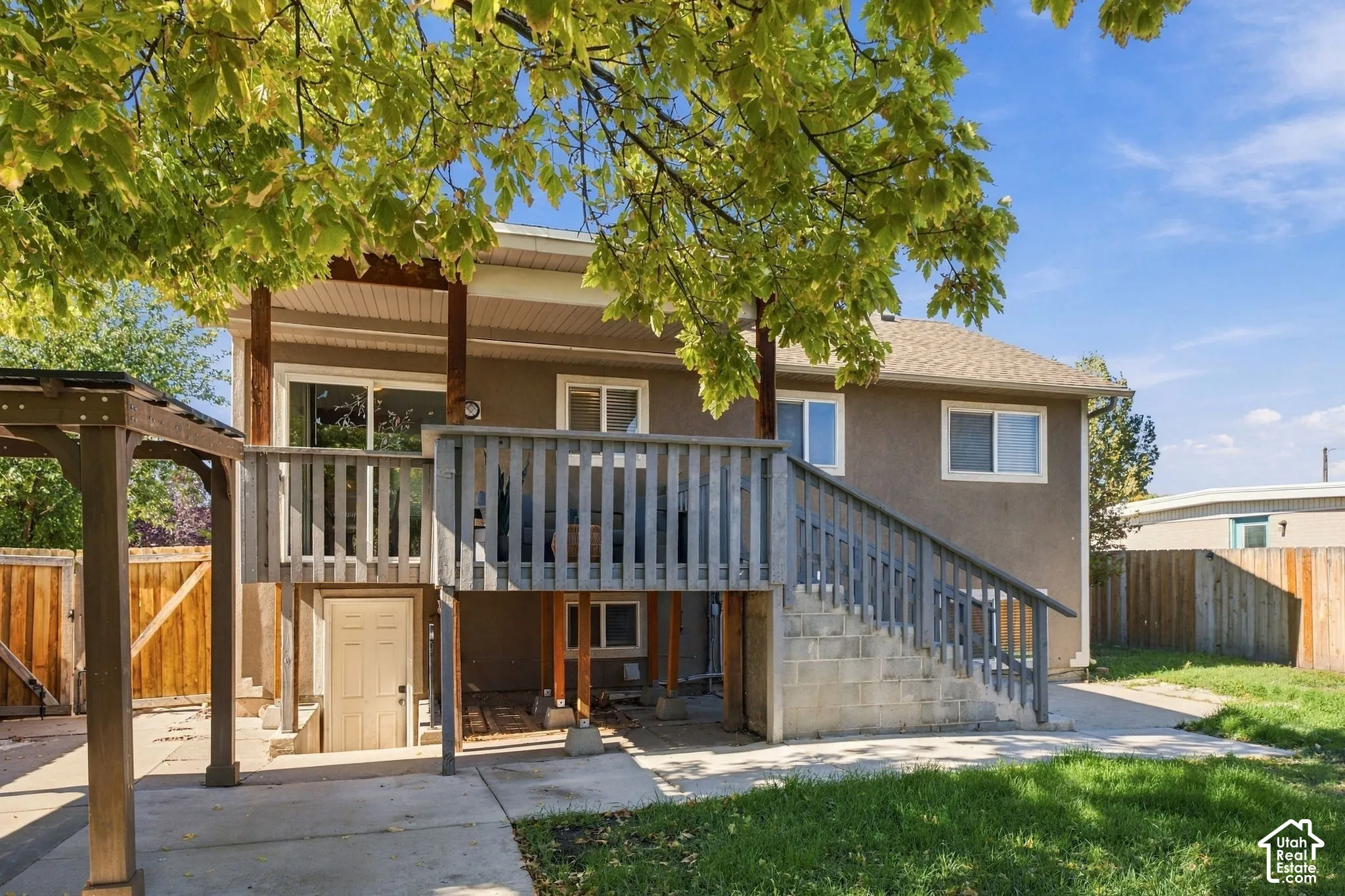 Rear exterior featuring a raised wood deck with staircase, concrete patio, detached wood-frame pergola, and perimeter wood fencing