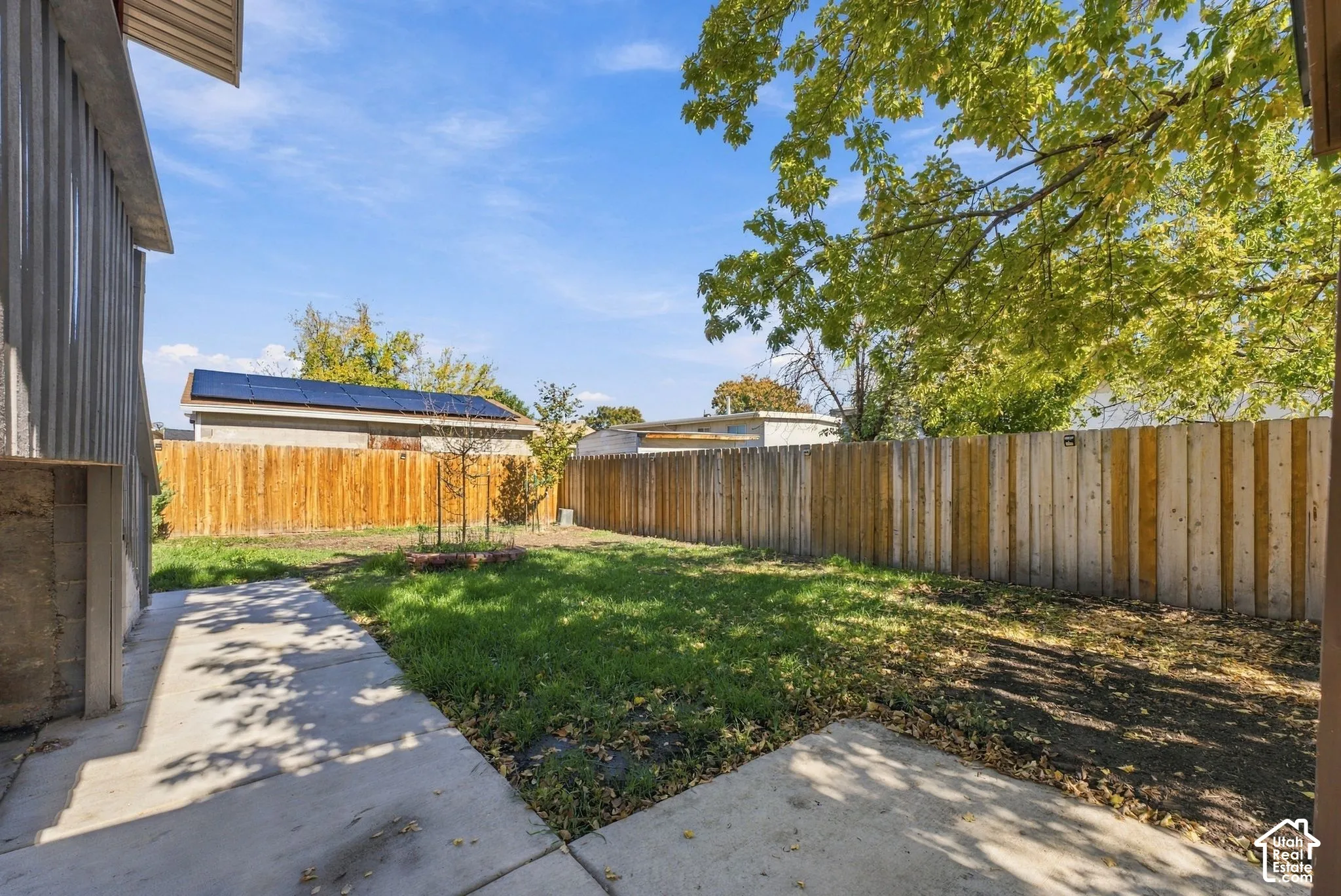 Private backyard featuring a concrete patio, grassy lawn, mature trees, and a full-height wood perimeter fence