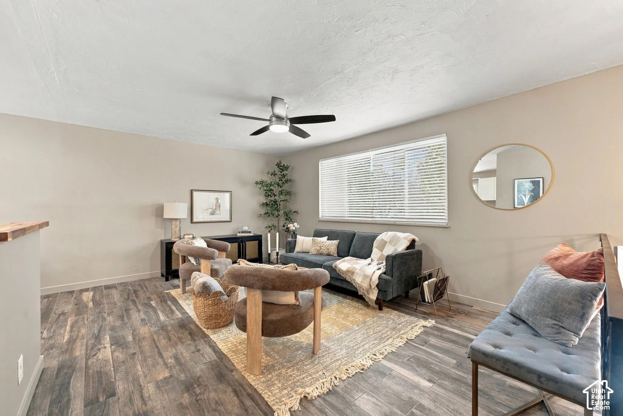 Neutral-toned interior space featuring wood-finish flooring, a ceiling fan with integrated lighting, and a horizontal window with adjustable blinds