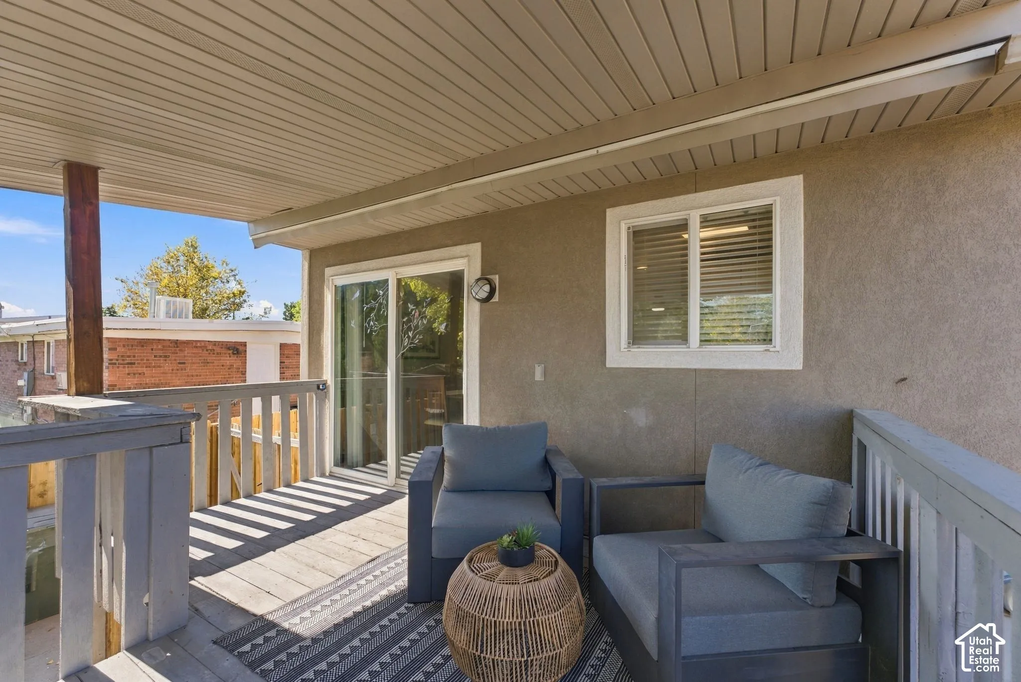 Covered exterior deck featuring a wooden railing, sliding glass door, and exterior wall-mounted lighting