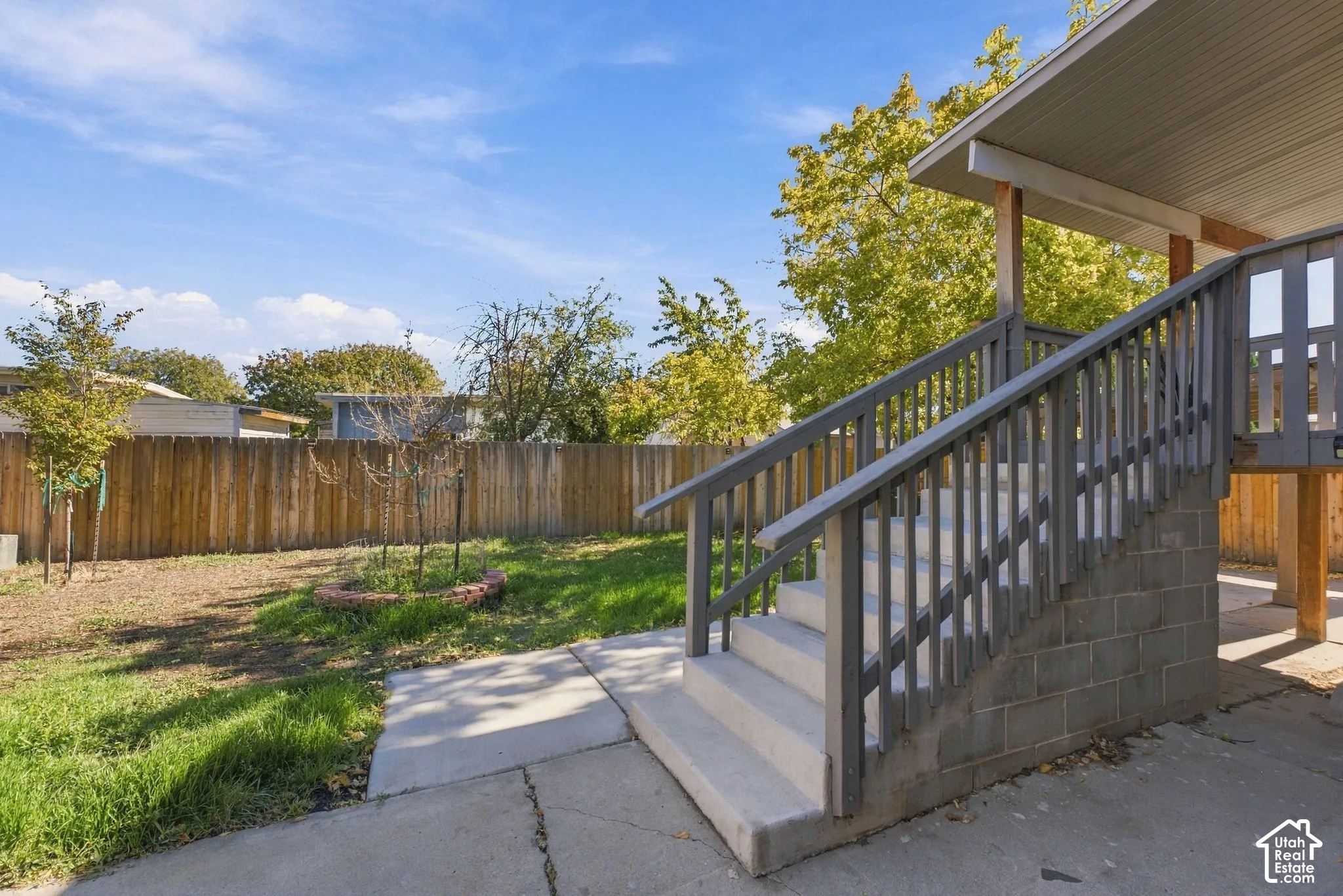 Backyard featuring a concrete patio, wood privacy fencing, a brick-edged planting bed, and a staircase with painted wood railings and concrete masonry unit base