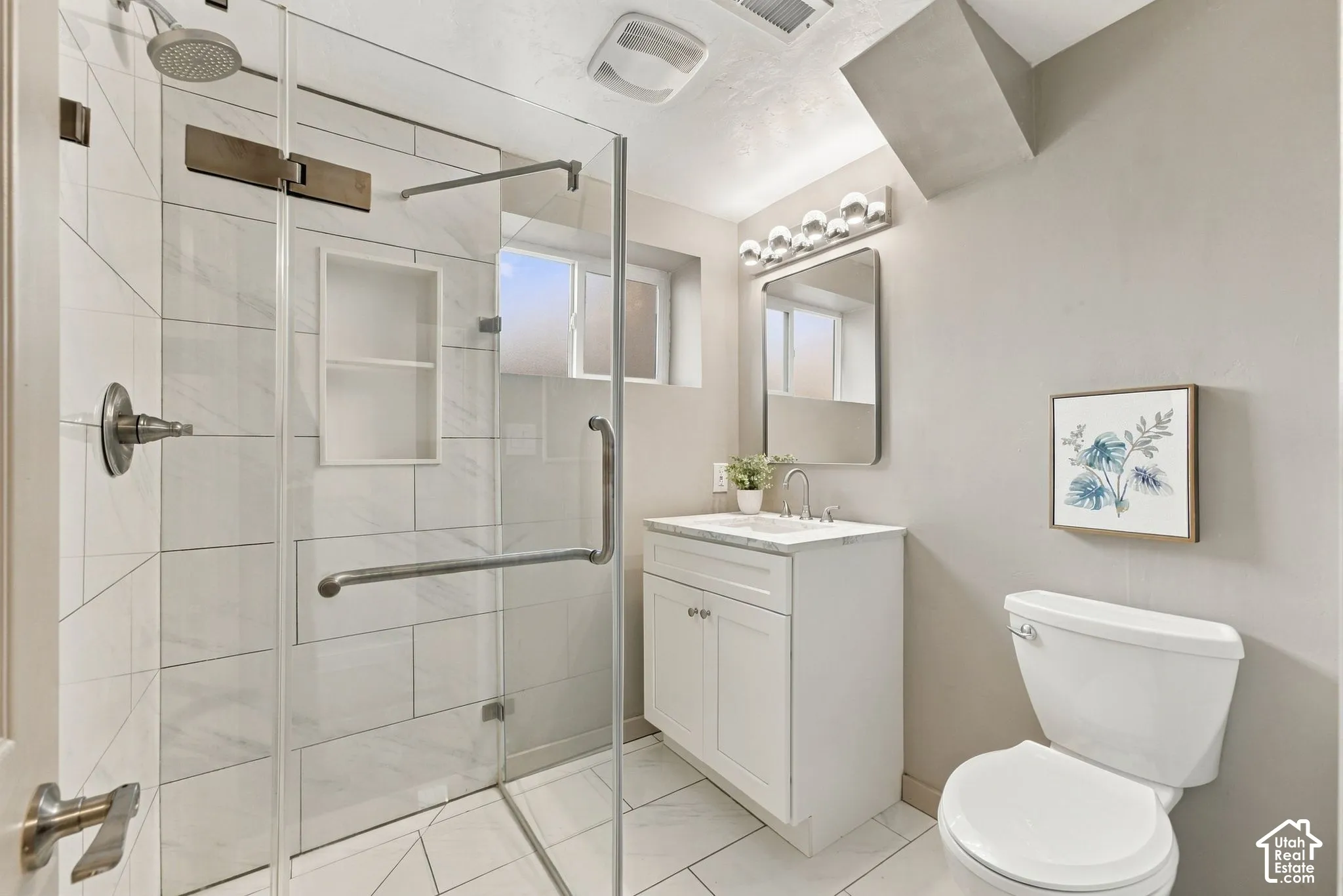 Walk-in shower with a glass enclosure, large-format tile surround, and recessed shelving, paired with a white shaker-style vanity featuring a stone countertop and a wall-mounted vanity mirror