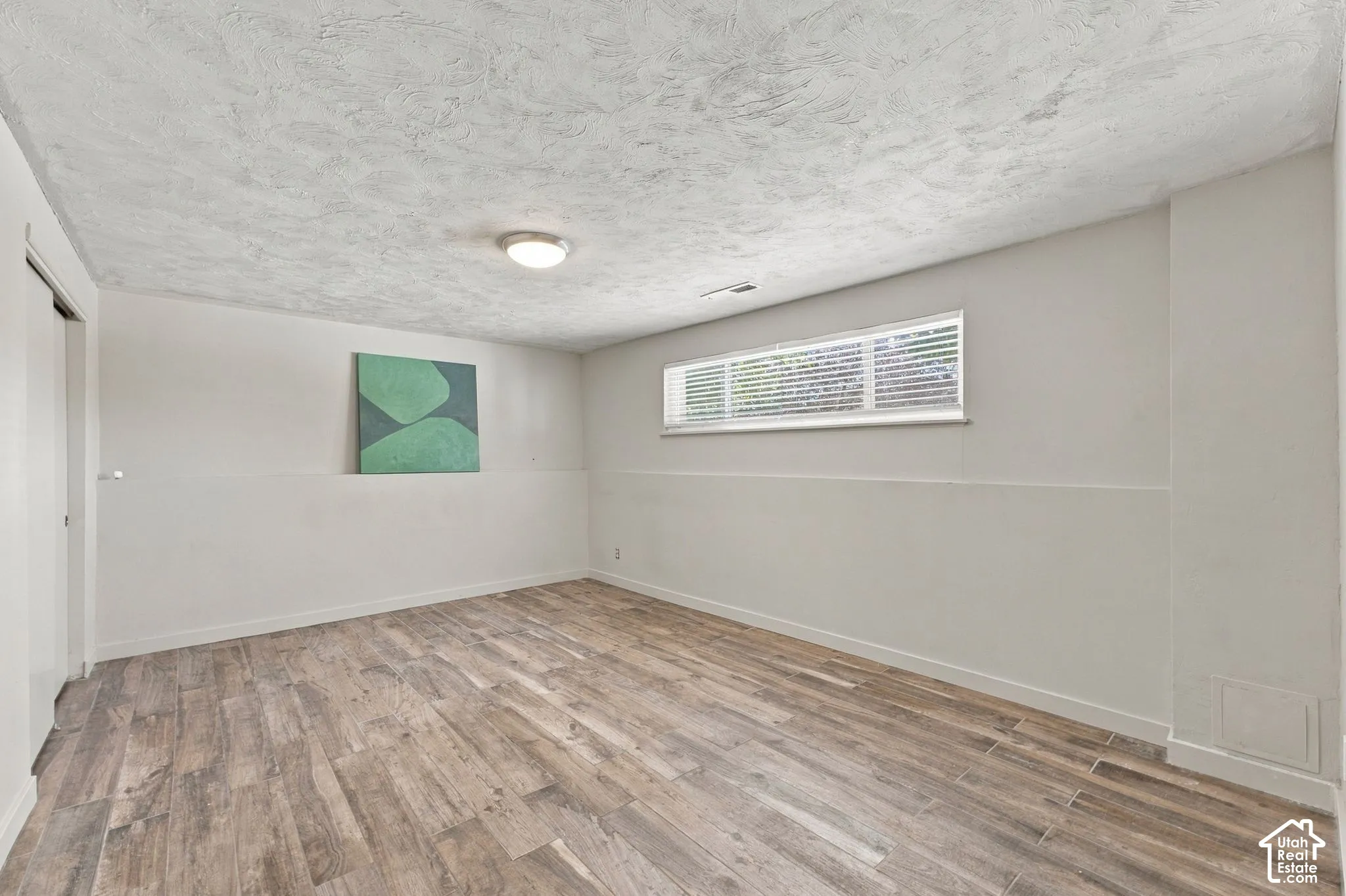 Room featuring wood-finish flooring, textured ceiling, horizontal sliding window, and neutral wall tones