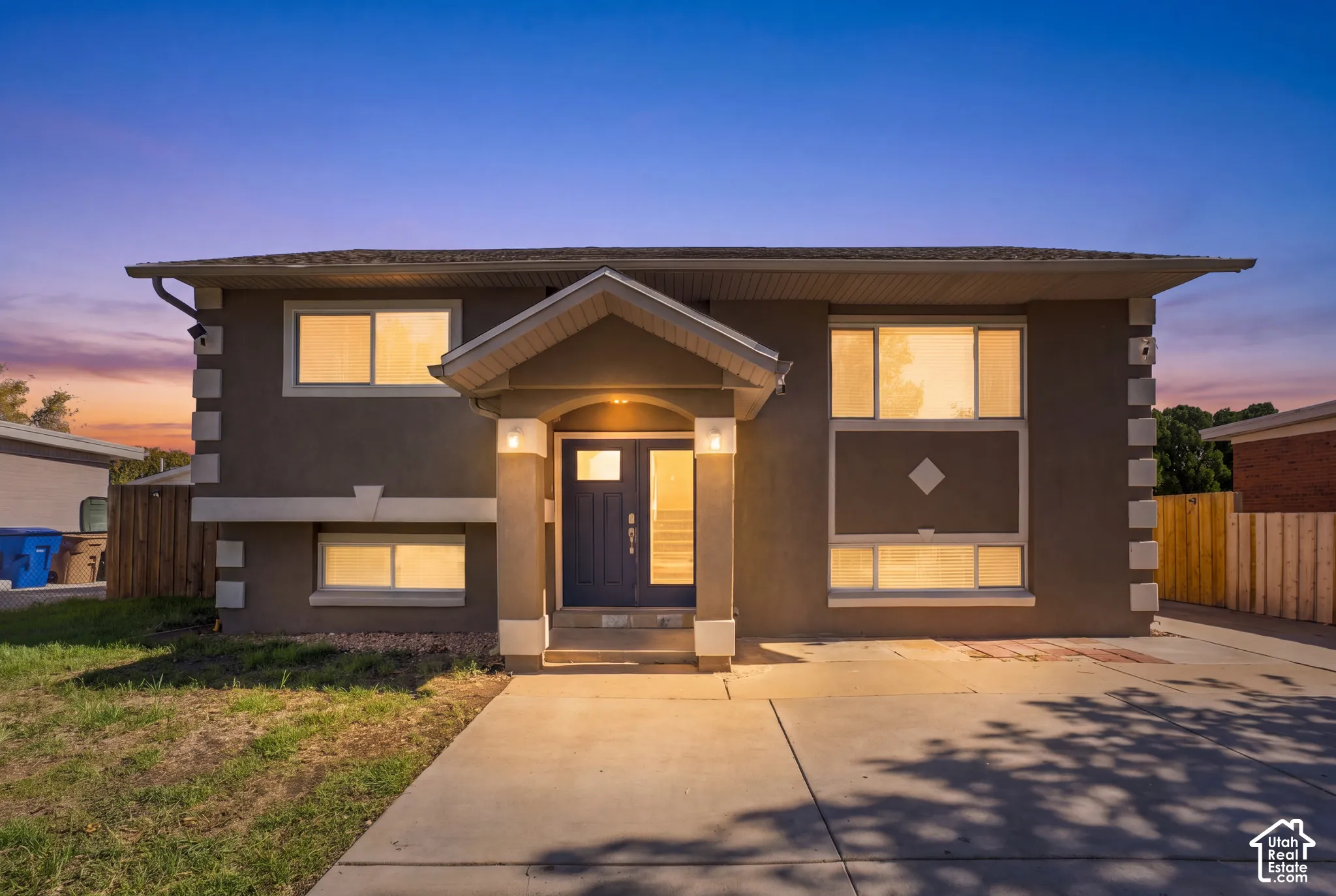 Exterior featuring stucco siding, stone-textured corner quoins, a covered entryway with a gabled roofline, double front entry doors, and a concrete driveway
