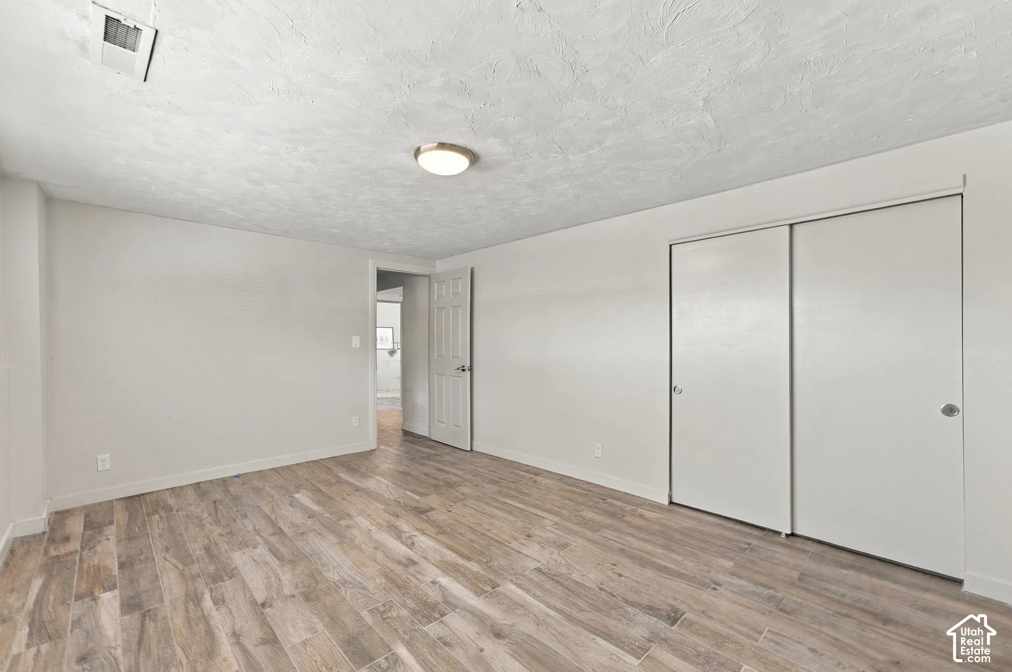 Wood-finish flooring, textured ceiling, flush-mount lighting, and dual sliding-door closet
