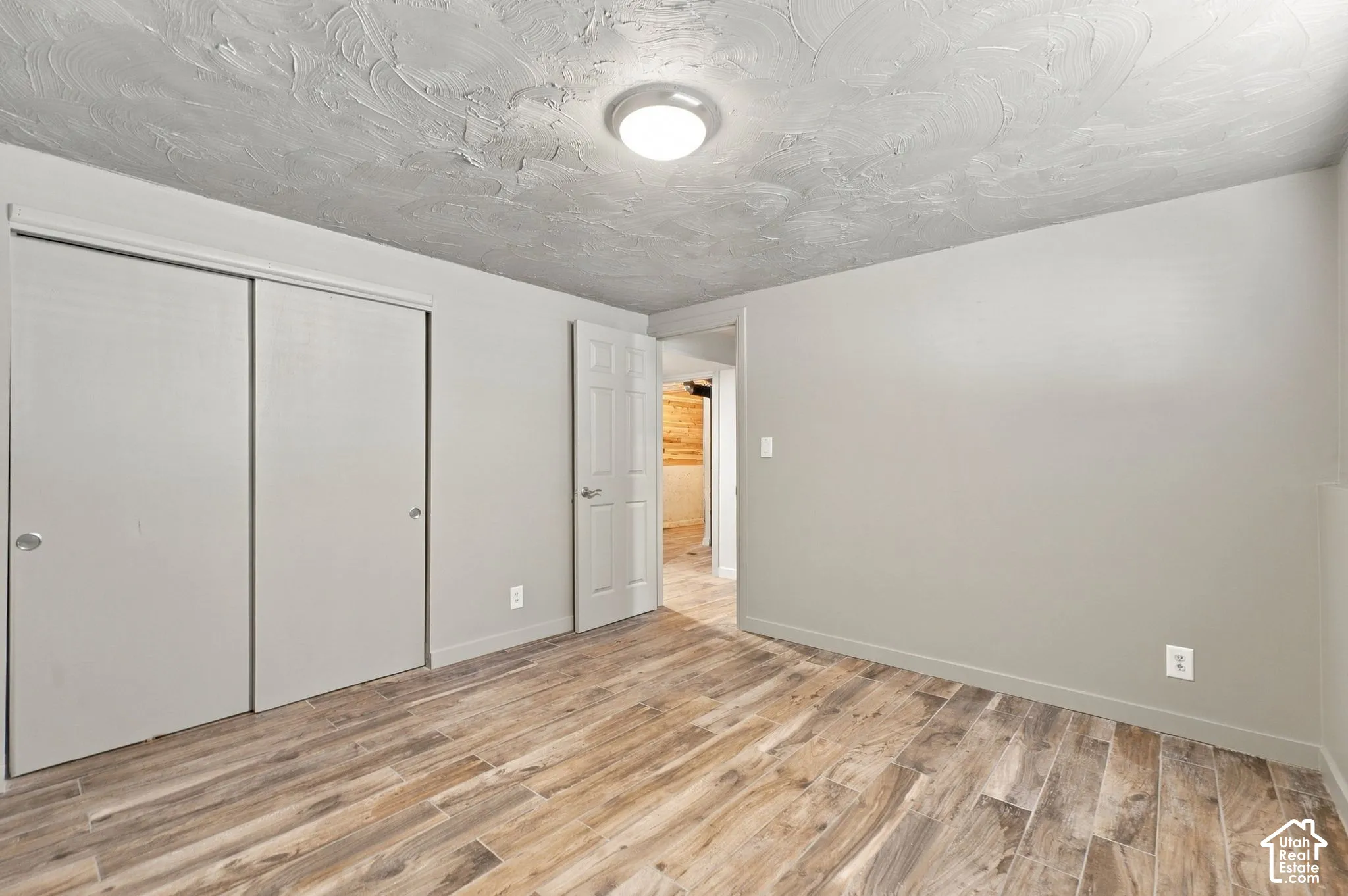 Room featuring wood-finish flooring, textured ceiling, flush-mount lighting, sliding closet doors, and a six-panel door