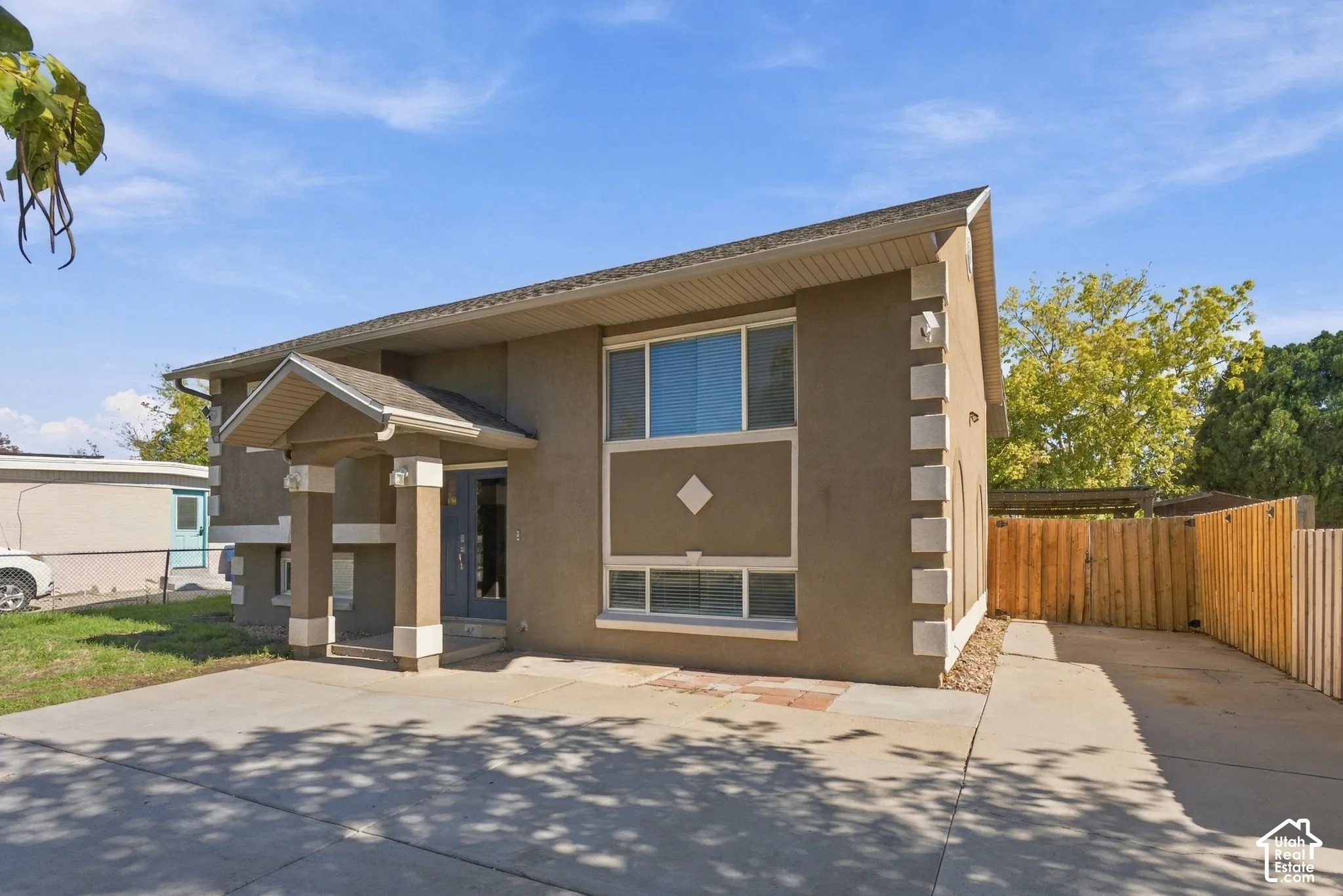 Stucco exterior featuring decorative corner quoins, a covered entryway with structural columns, multi-pane windows, and a concrete driveway