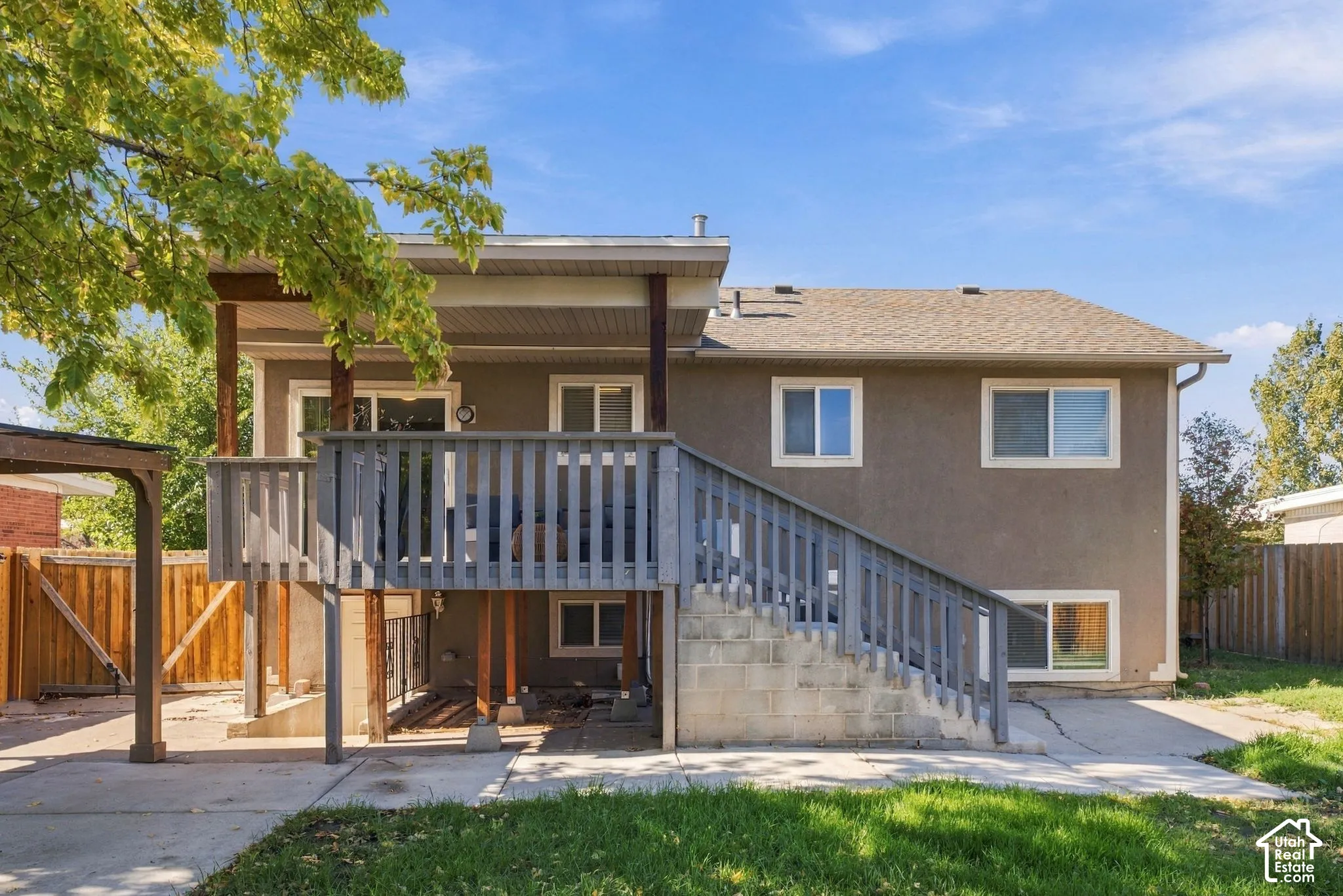 Stucco exterior featuring a raised wooden deck with staircase, concrete patio, and fenced yard