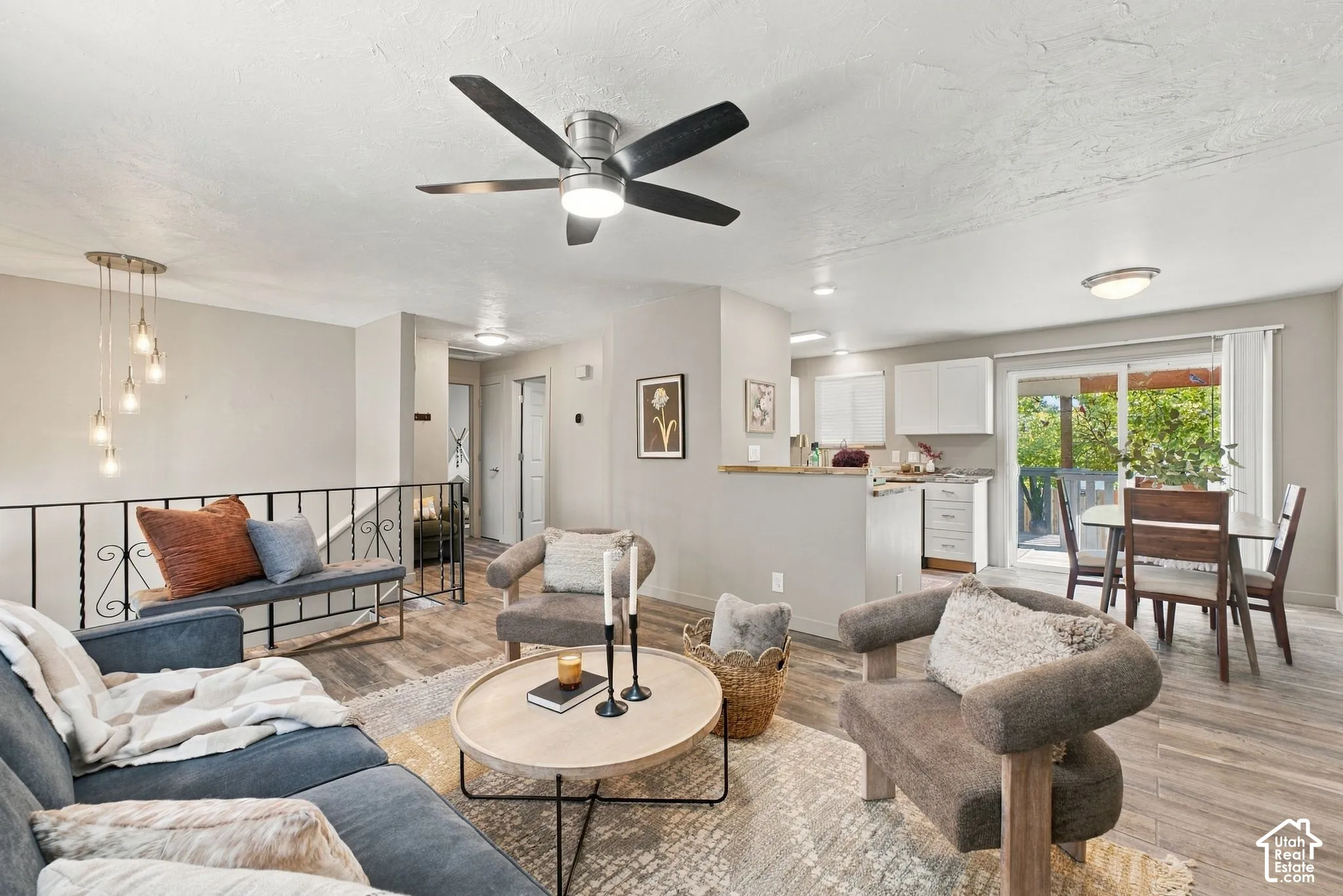 Open-concept main living area featuring wood-finish flooring, a contemporary ceiling fan, decorative metal railing, and sliding glass doors