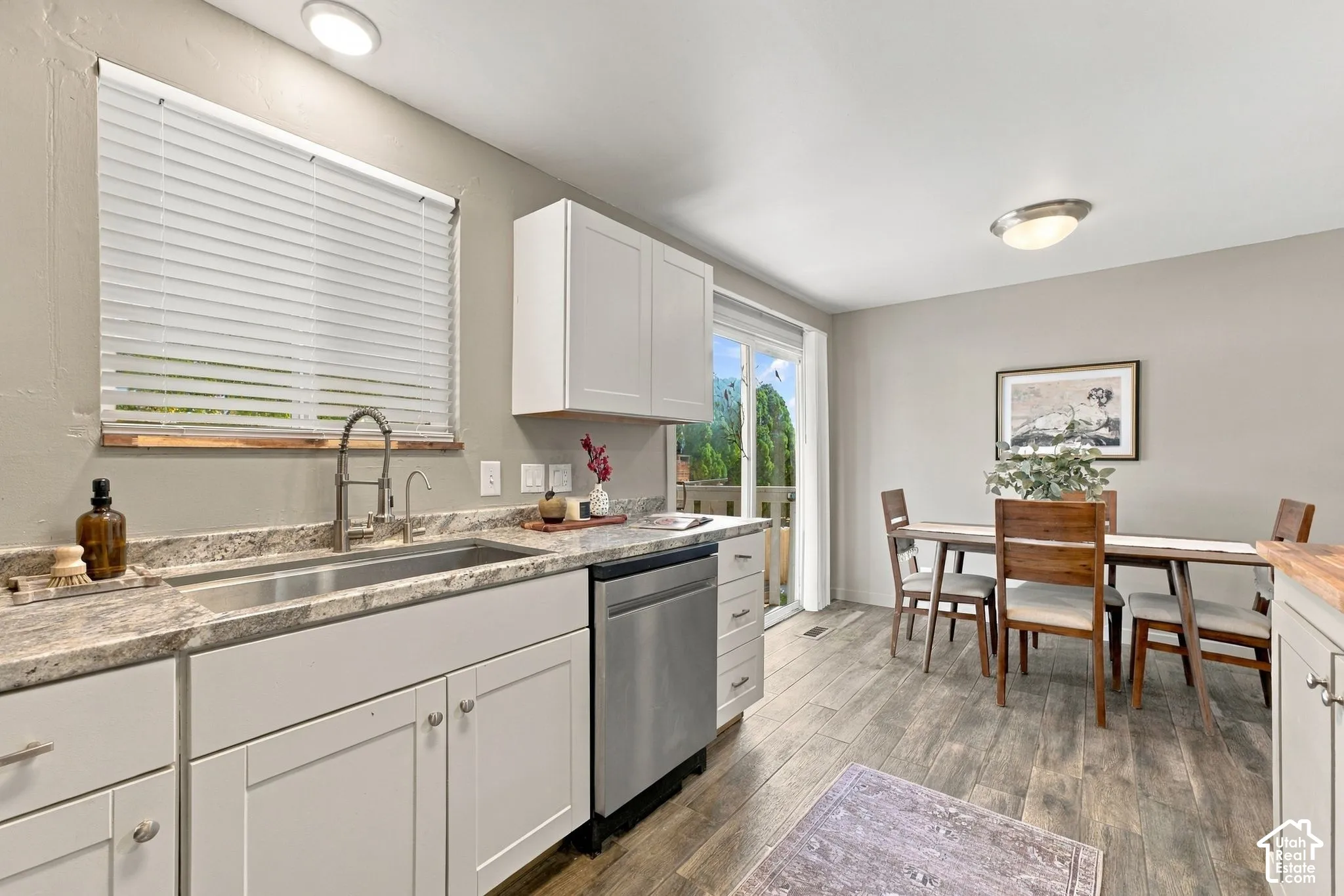 Kitchen featuring white cabinetry, stone-finish countertops, stainless steel dishwasher, high-arc faucet, and wood-finish flooring