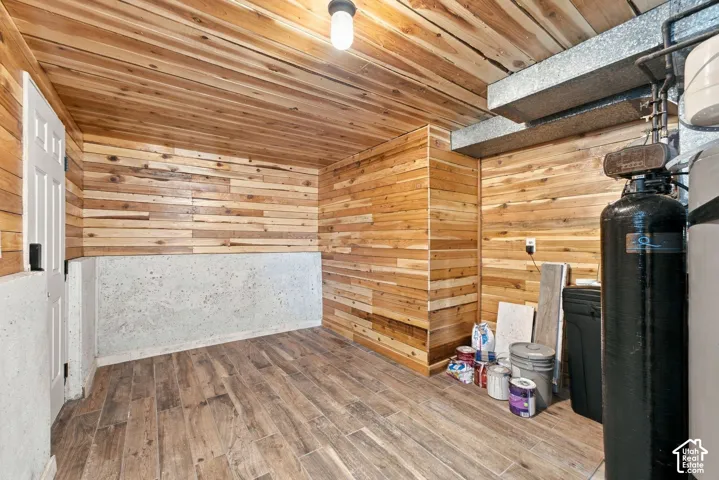Utility room featuring tongue-and-groove wood wall paneling, wood-finish tile flooring, a six-panel door, and an exposed ceiling structure