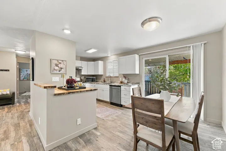 Kitchen featuring white cabinetry, wood-finish flooring, a butcher-block style countertop island, stainless steel dishwasher, and sliding glass doors
