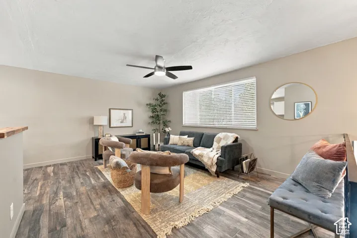 Neutral-toned interior space featuring wood-finish flooring, a ceiling fan with integrated lighting, and a horizontal window with adjustable blinds