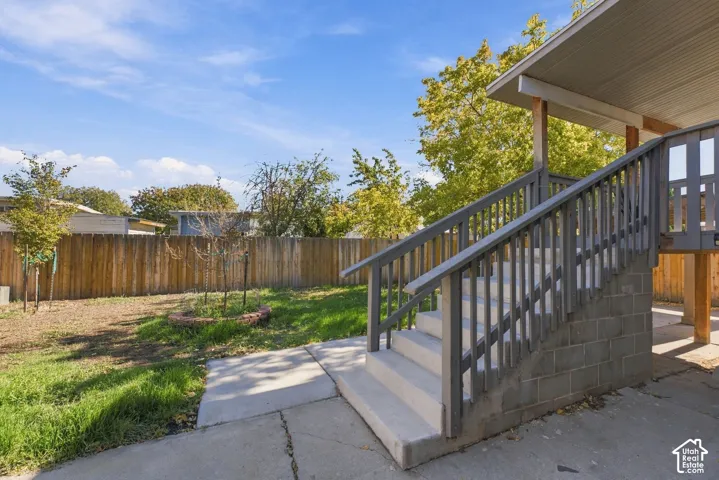 Backyard featuring a concrete patio, wood privacy fencing, a brick-edged planting bed, and a staircase with painted wood railings and concrete masonry unit base