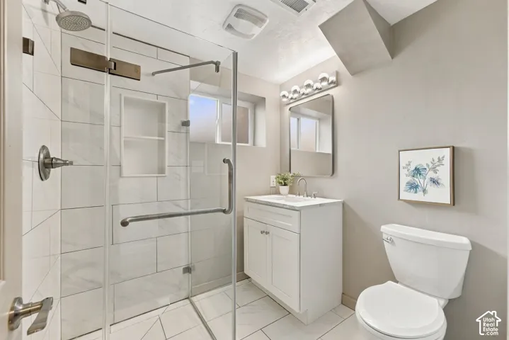 Walk-in shower with a glass enclosure, large-format tile surround, and recessed shelving, paired with a white shaker-style vanity featuring a stone countertop and a wall-mounted vanity mirror