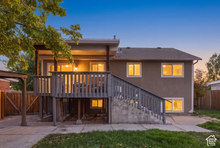 Stucco exterior featuring an elevated wood deck with stairs, a concrete block foundation, and a concrete patio