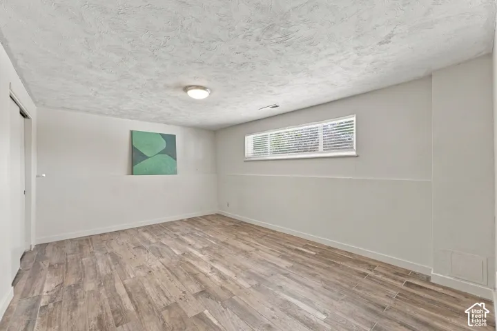 Room featuring wood-finish flooring, textured ceiling, horizontal sliding window, and neutral wall tones