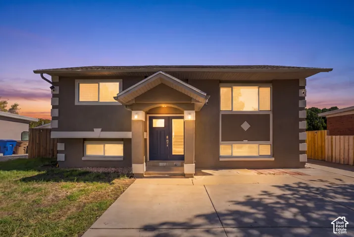 Exterior featuring stucco siding, stone-textured corner quoins, a covered entryway with a gabled roofline, double front entry doors, and a concrete driveway