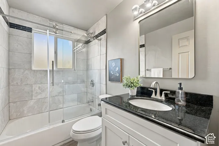 Bathroom featuring a stone-tile tub surround with an integrated dark decorative accent tile, sliding glass shower door, dark stone countertop with an undermount sink, and a rectangular mirror with rounded corners