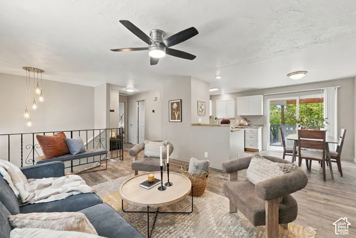 Open-concept main living area featuring wood-finish flooring, a contemporary ceiling fan, decorative metal railing, and sliding glass doors