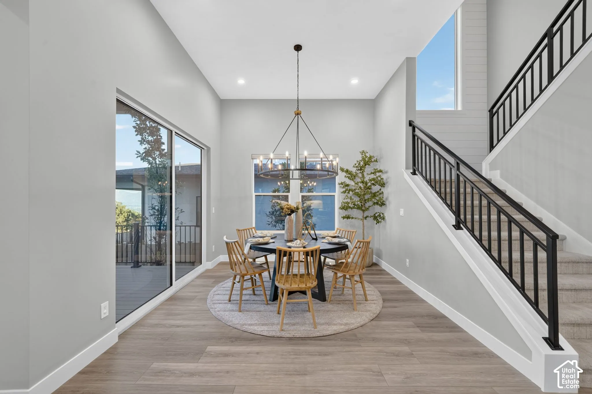 High-ceiling interior featuring wood-finish flooring, a contemporary multi-arm chandelier, large sliding glass doors, and a staircase with a matte black metal railing