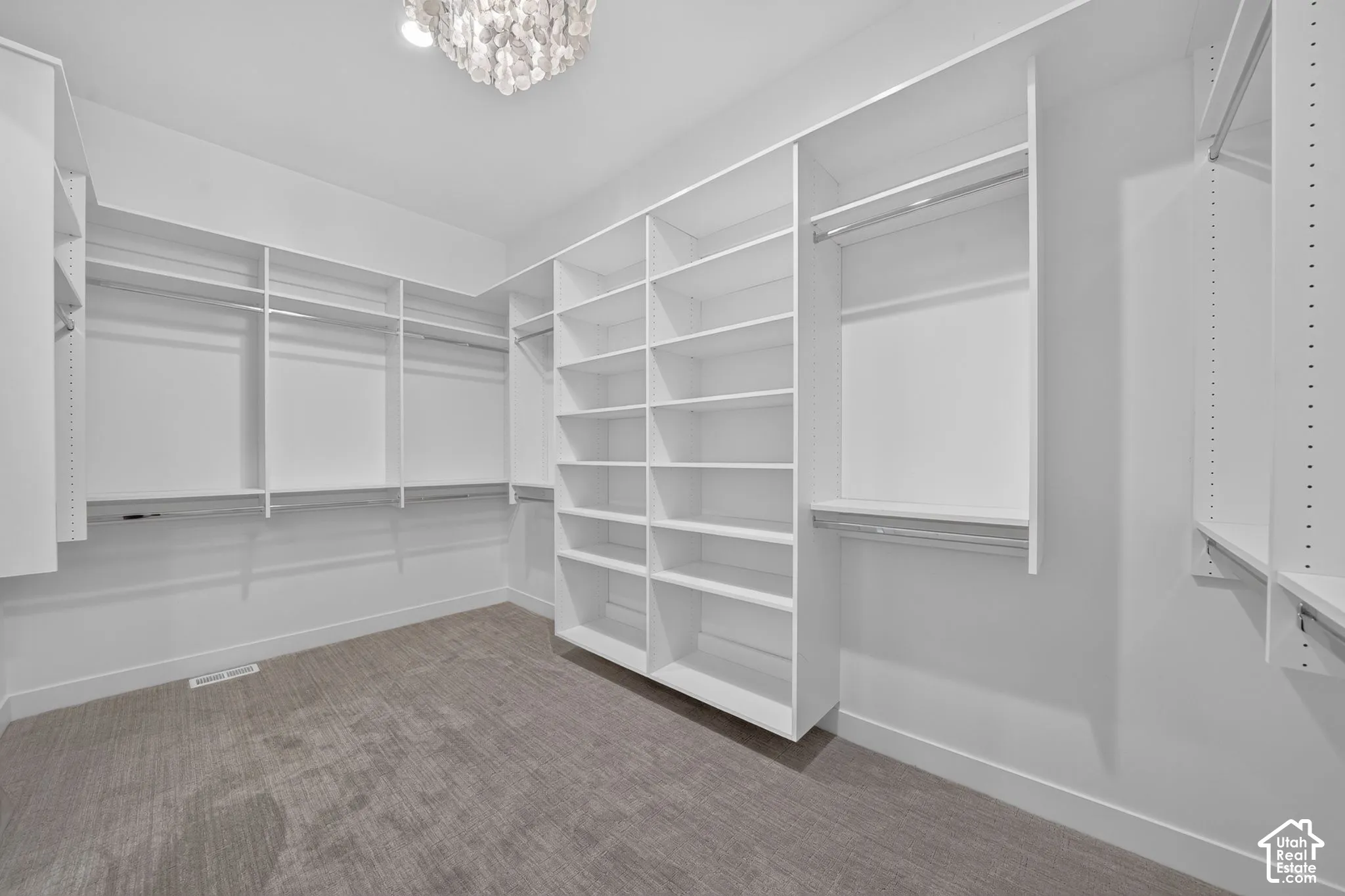 Walk-in closet featuring floor-to-ceiling custom white shelving, multiple hanging rods, wall-to-wall carpeting, and a decorative overhead light fixture