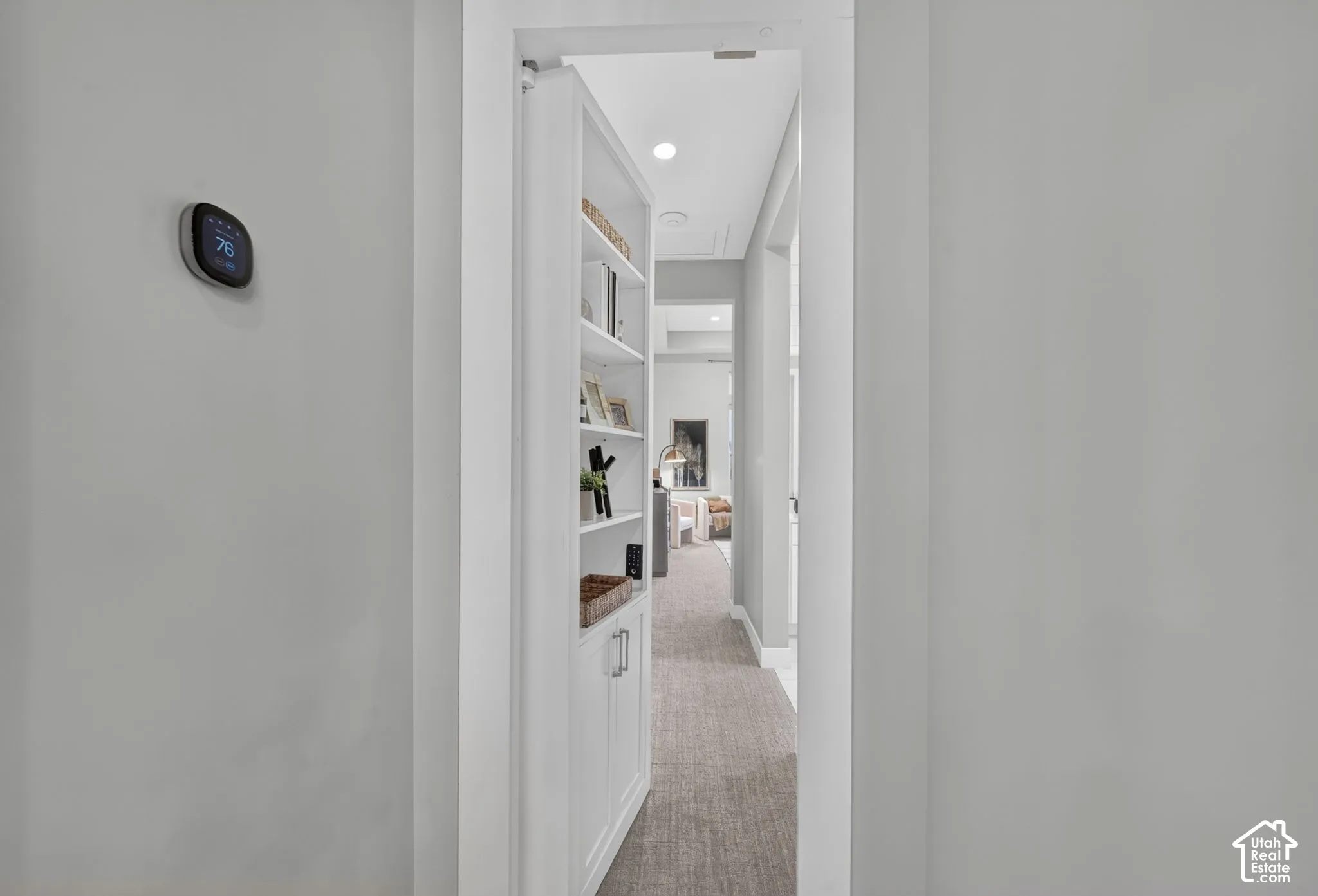 Built-in white cabinetry featuring a concealed door panel, smart home thermostat, and recessed ceiling lighting