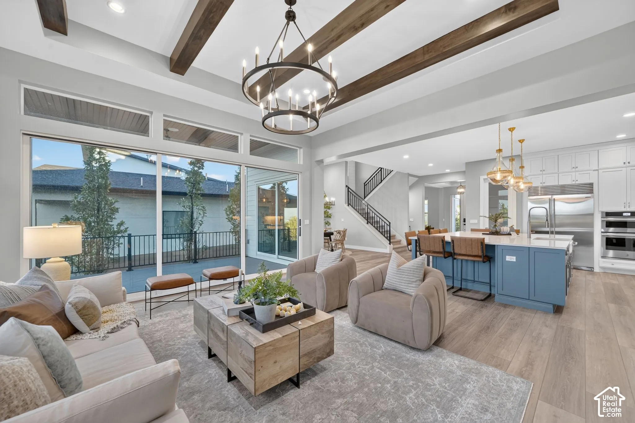 Open-concept floor plan featuring exposed wood ceiling beams, floor-to-ceiling sliding glass doors, custom white cabinetry, and wood-finish flooring