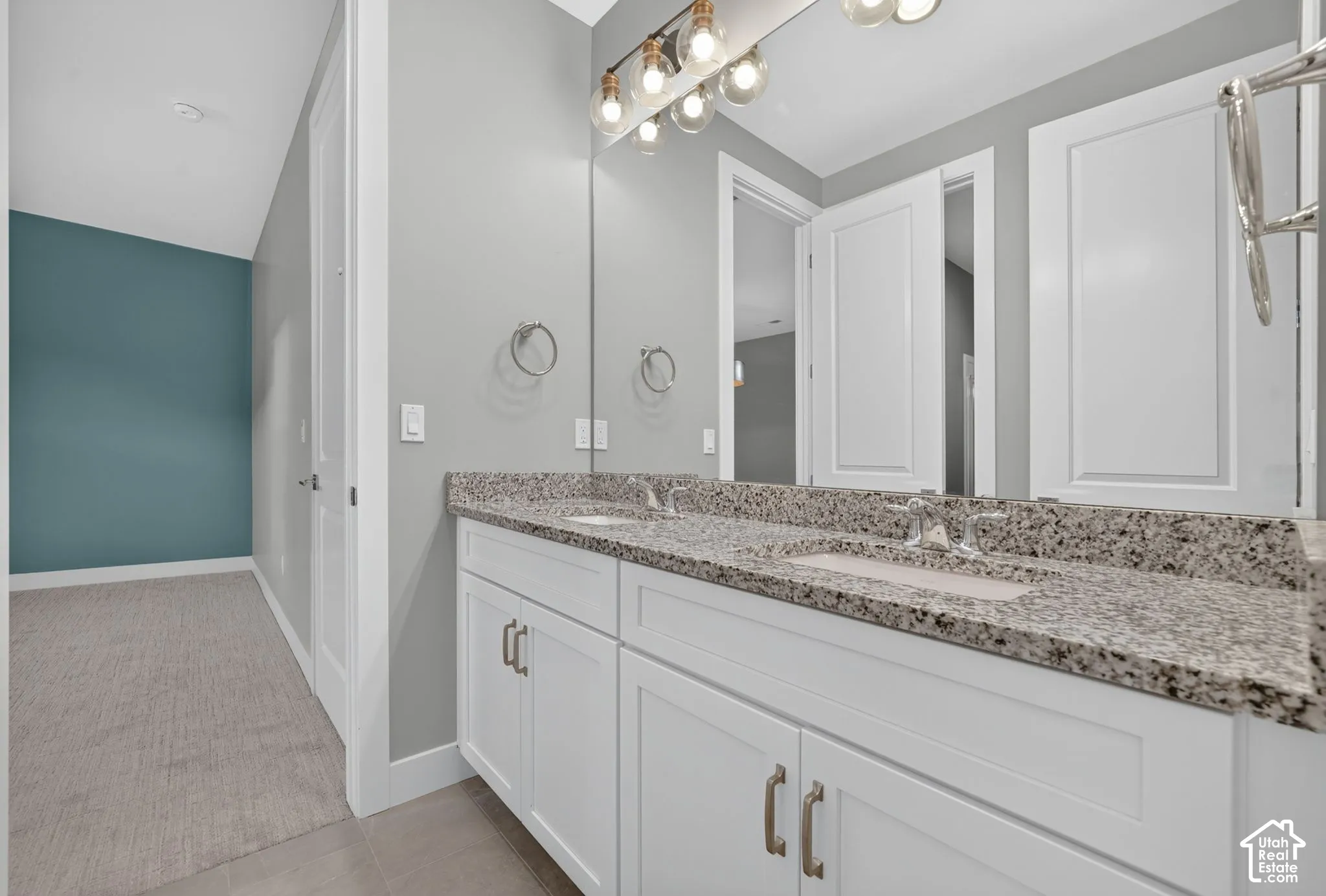Double vanity with stone-surface countertop, dual integrated rectangular sinks, white shaker-style cabinetry, and multi-bulb linear vanity lighting