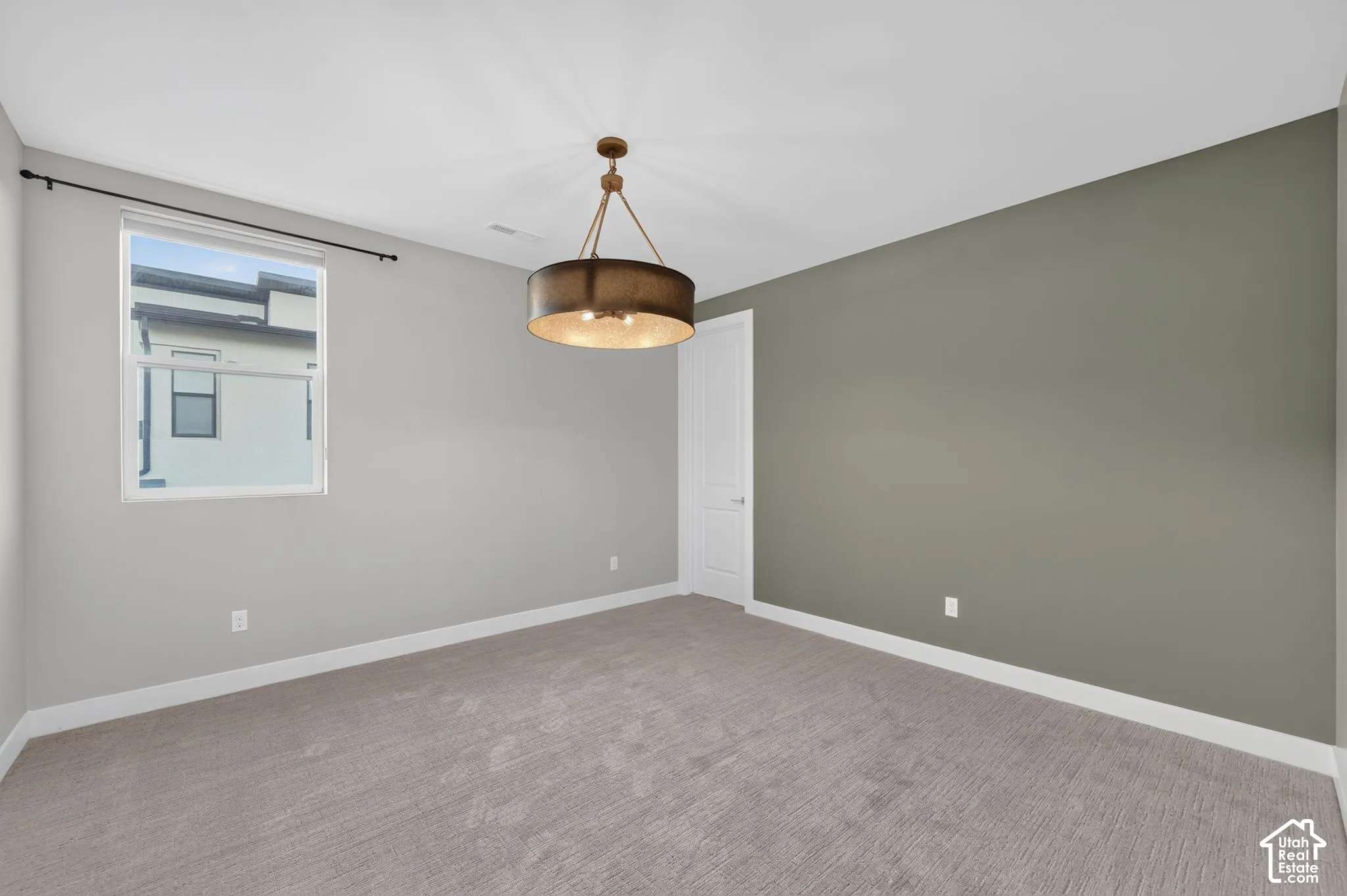Room featuring neutral carpeting, an olive-tone accent wall, a drum-style pendant light fixture, and a single-pane window