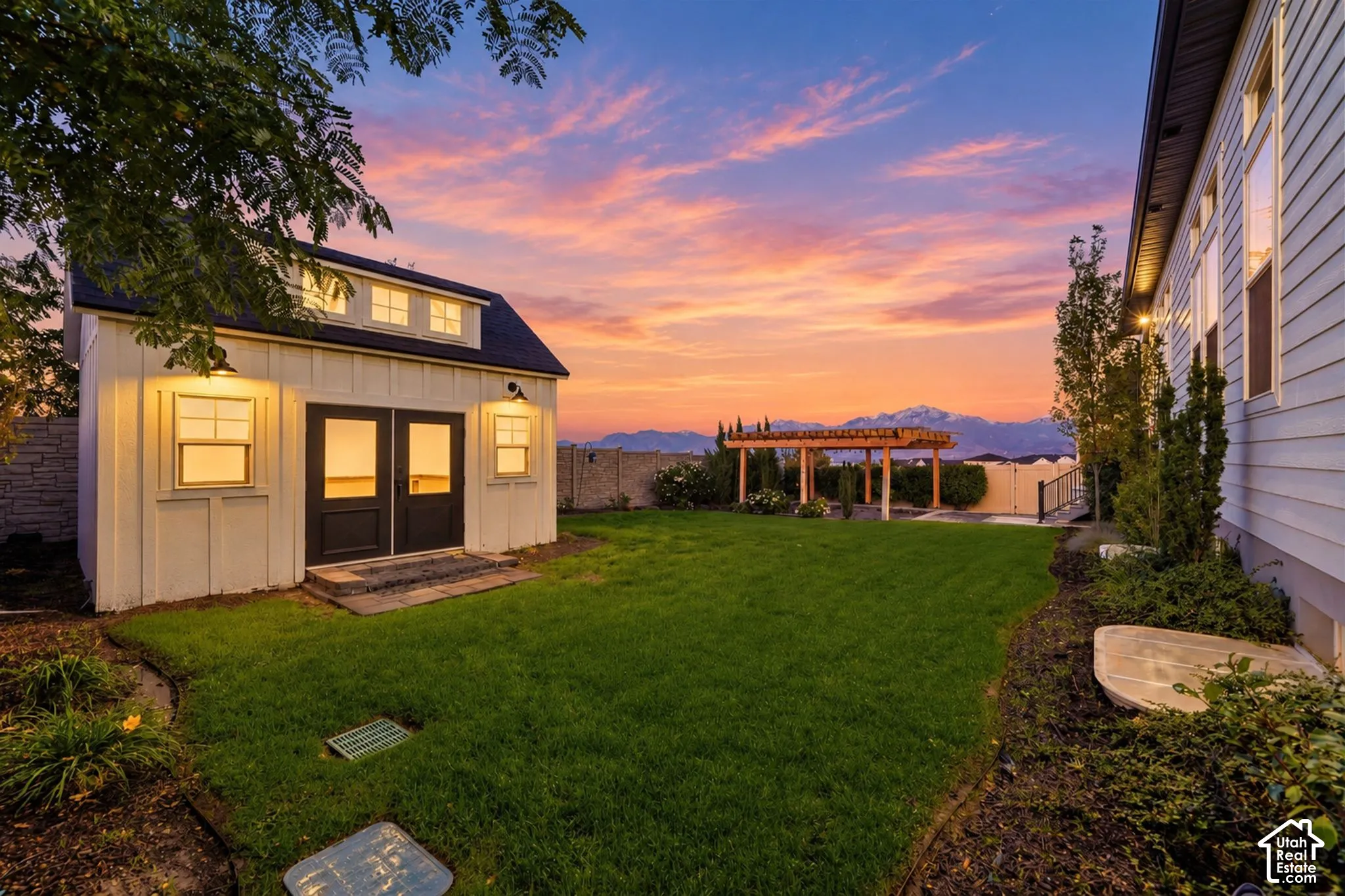 Backyard featuring a detached outbuilding with a dormer, manicured lawn, wood-framed pergola, and mountain backdrop