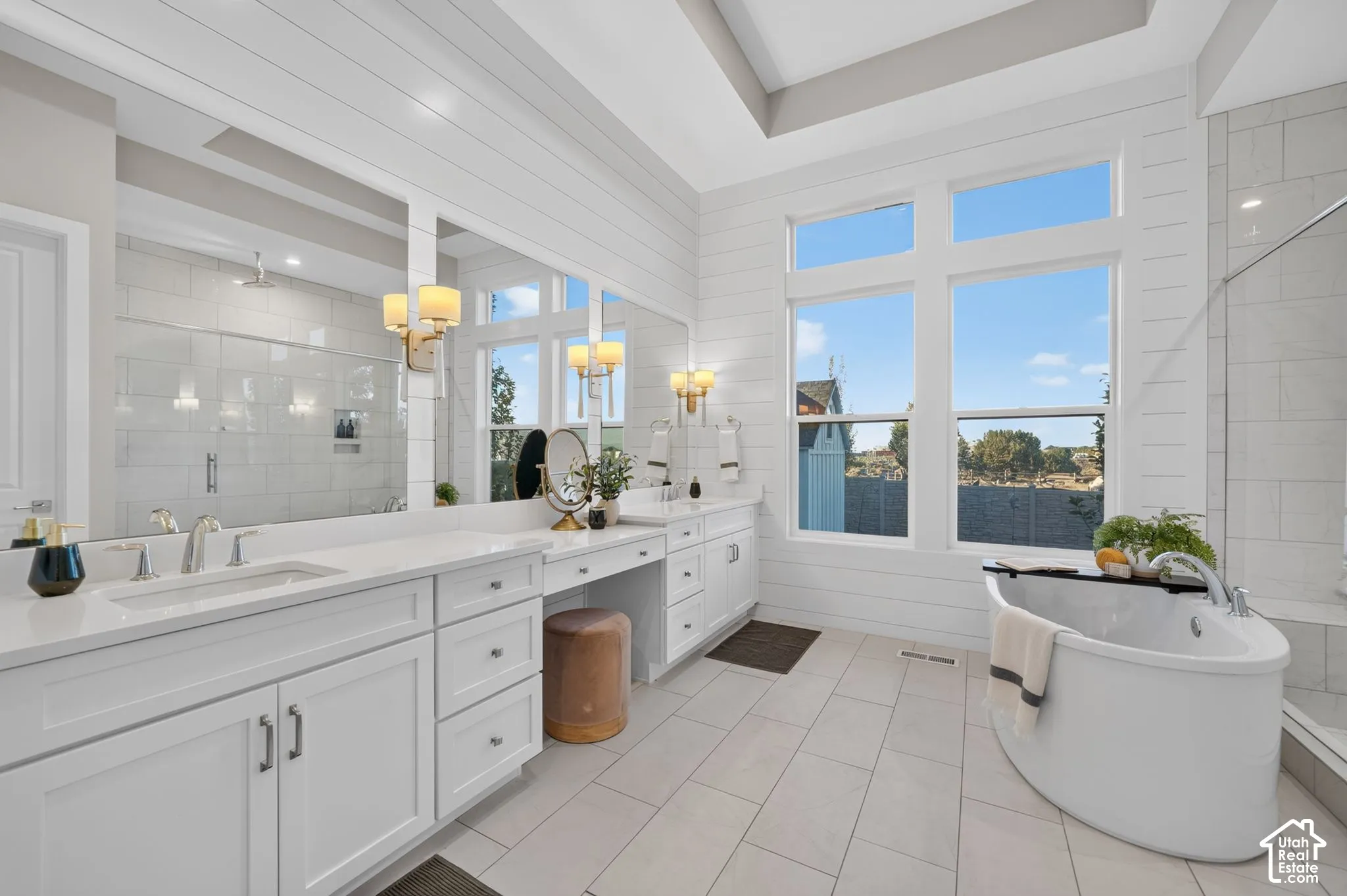 Bathroom featuring shiplap walls, a dual-sink vanity with stone-surfaced countertops, a freestanding soaking tub, and large-format tile flooring
