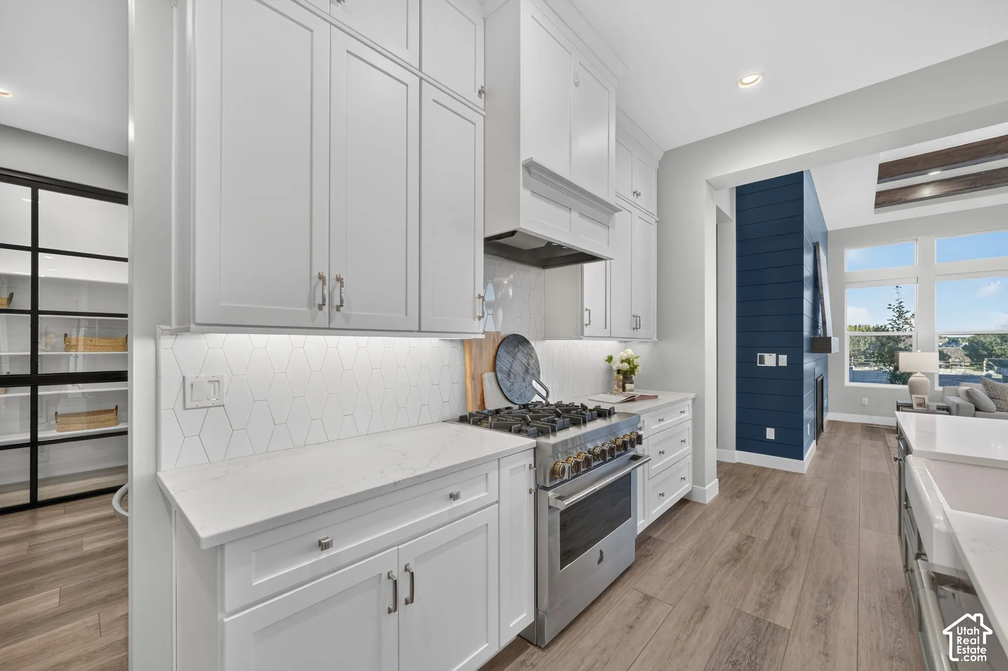 Kitchen featuring white shaker-style cabinetry, quartz countertops, a stainless steel gas range with a custom hood, hexagon-patterned tile backsplash, and wood-finish flooring