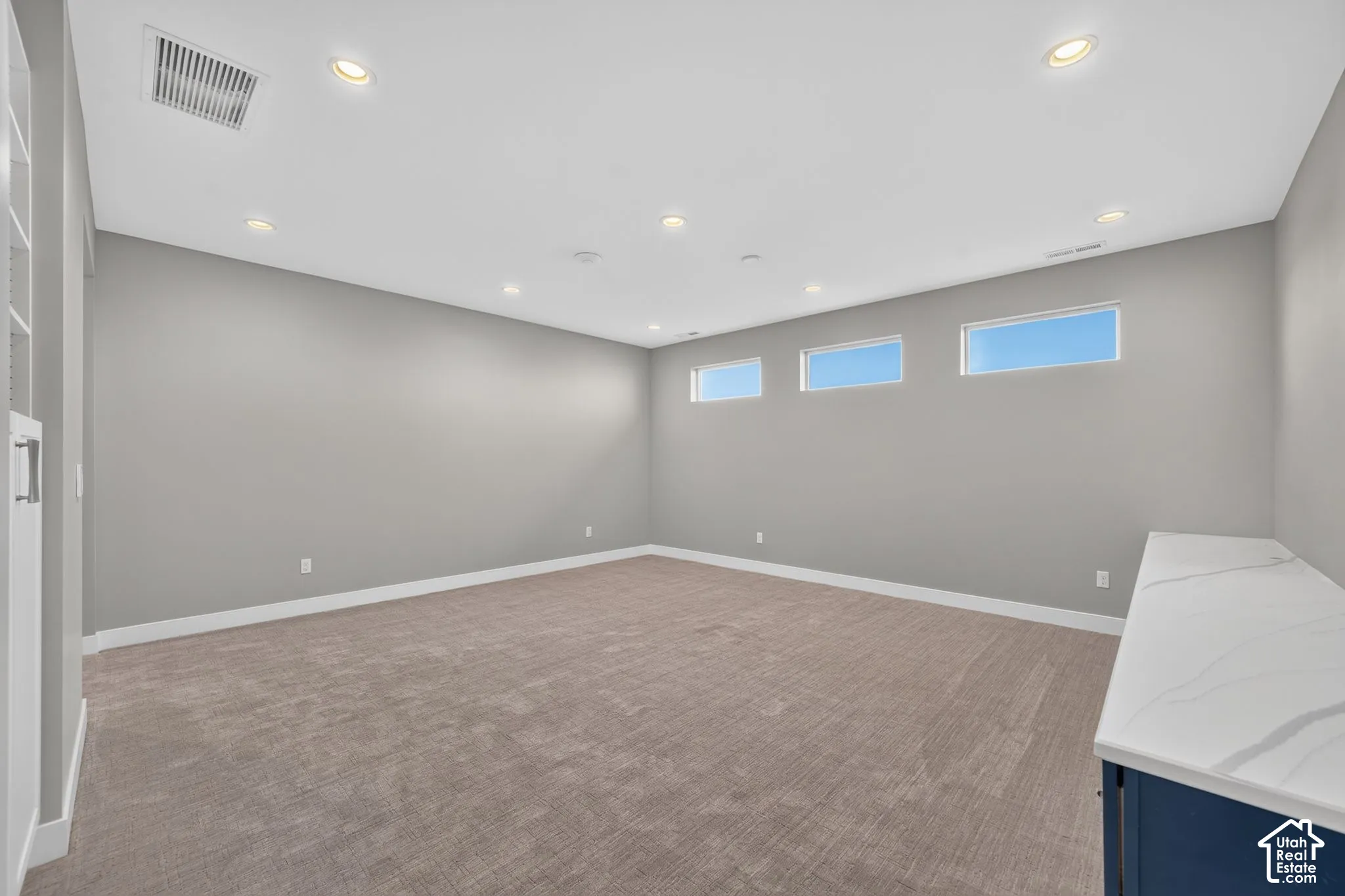Room featuring recessed lighting, carpeted flooring, three high-set rectangular windows, and a built-in cabinet with a stone-finish countertop