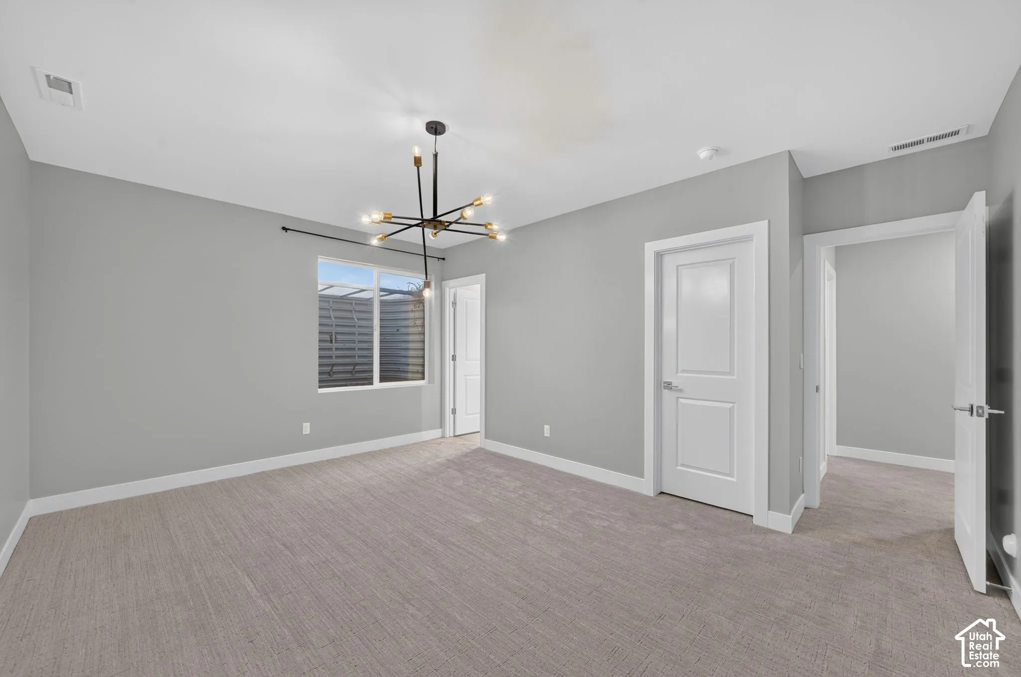 Neutral-toned wall paint, neutral carpeting, multi-arm sputnik-style chandelier, single-hung window with a metal curtain rod, and three-panel interior doors
