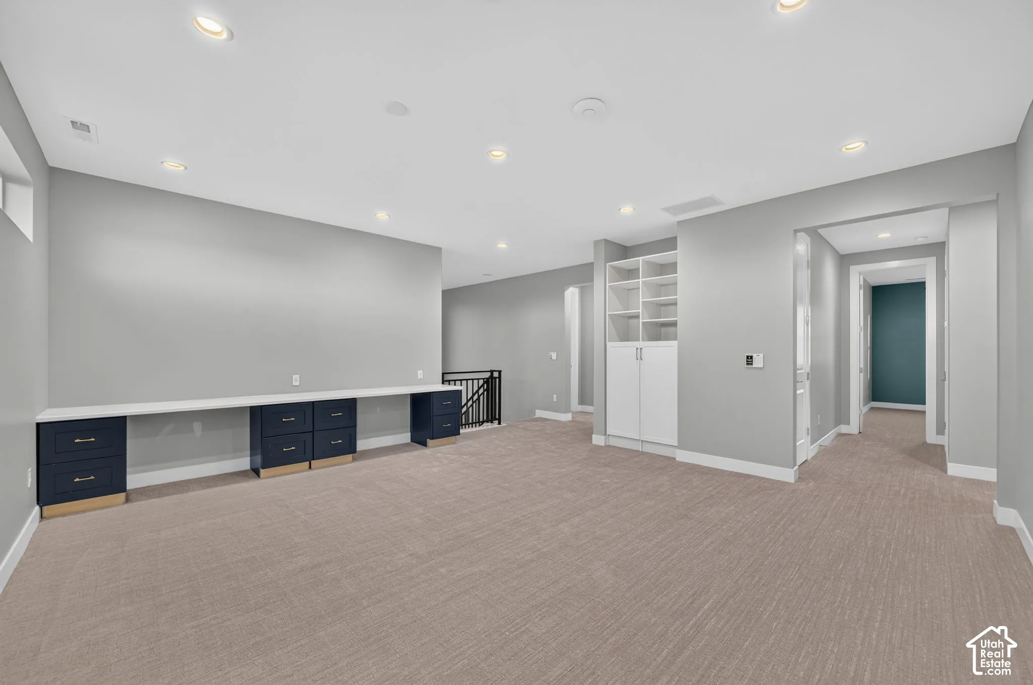 Open-concept area featuring neutral carpeting, recessed lighting, built-in desk cabinetry with a solid surface countertop, and floor-to-ceiling shelving