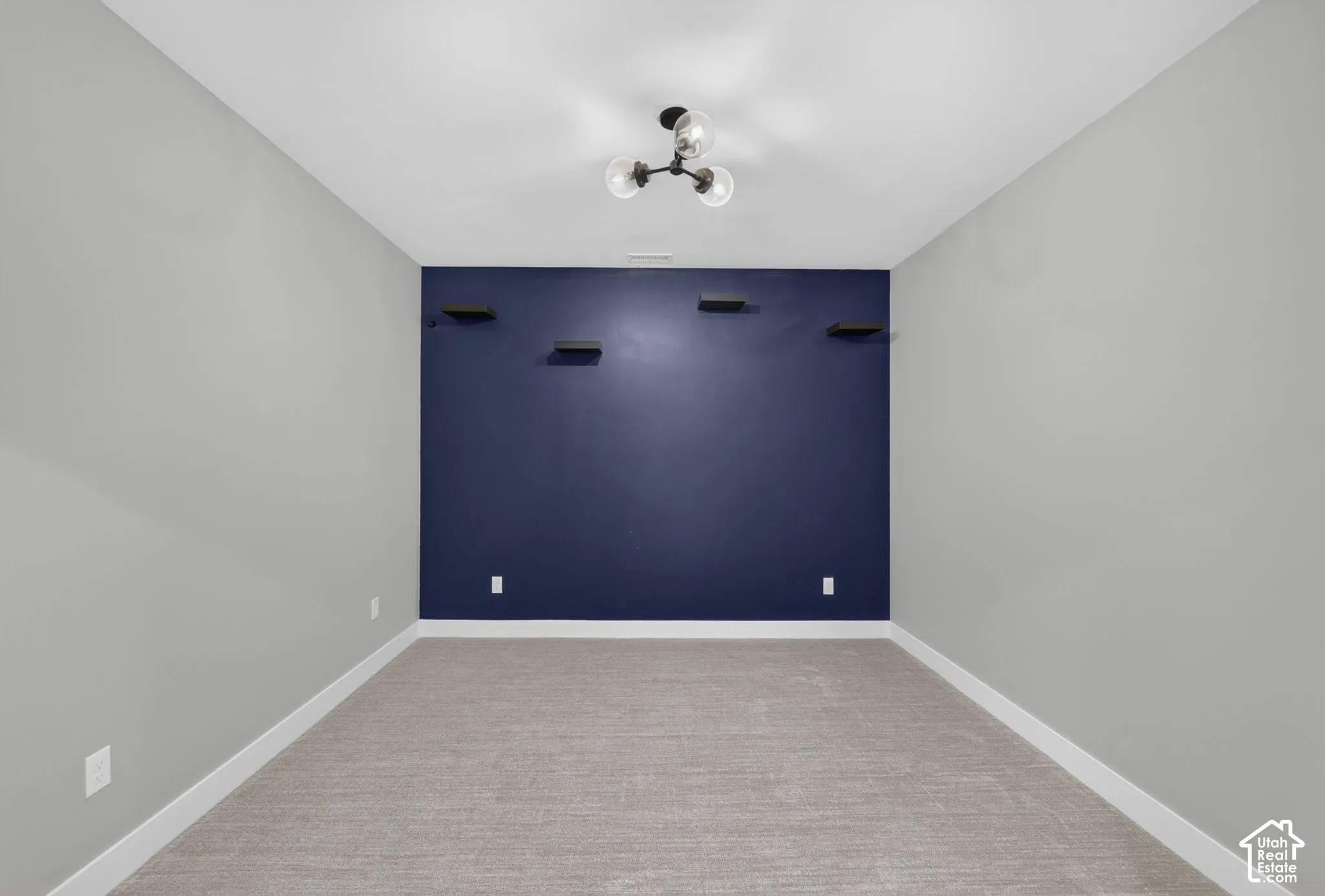 Room featuring an accent wall, four built-in floating shelves, neutral wall-to-wall carpeting, and a multi-bulb flush-mount light fixture
