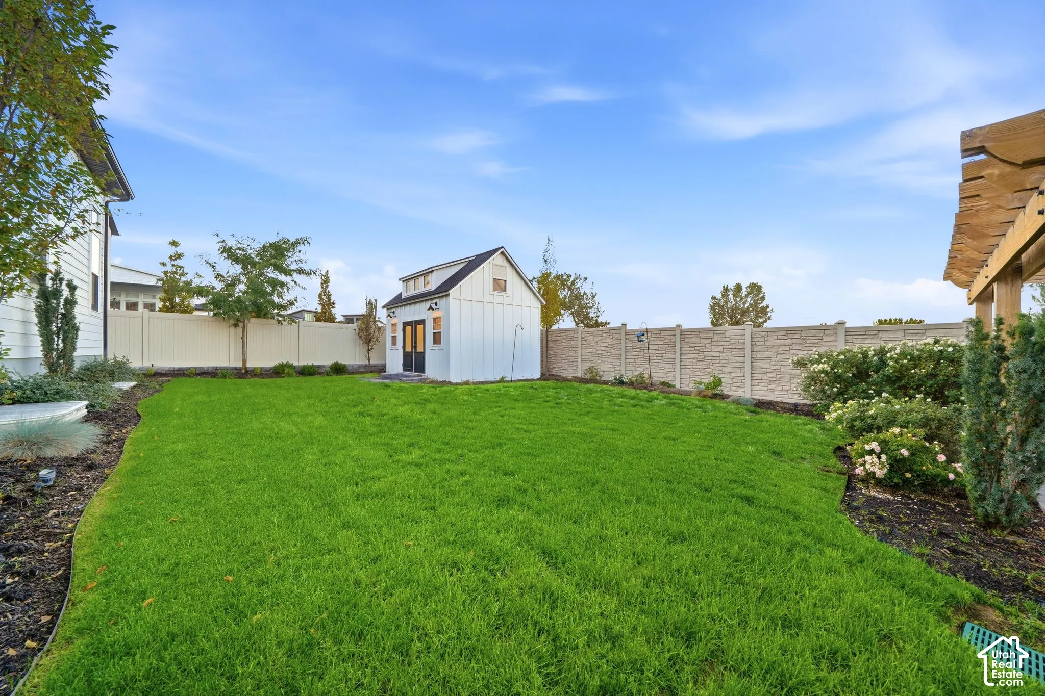 Backyard featuring a manicured lawn, detached board-and-batten storage structure, perimeter privacy fencing, and wood-beam pergola