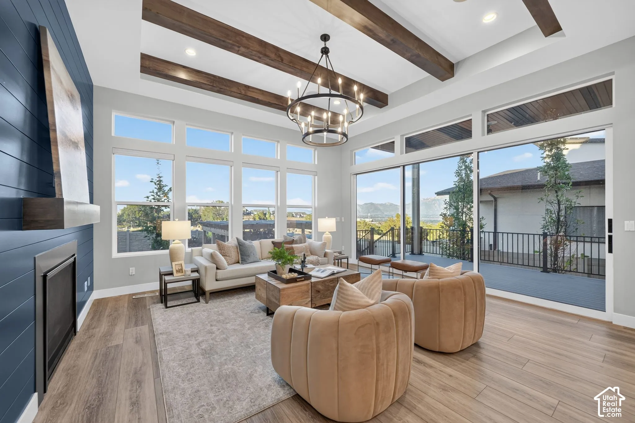 Coffered ceiling with exposed wood beams, floor-to-ceiling windows, blue shiplap accent wall with integrated fireplace, and multi-panel sliding glass doors