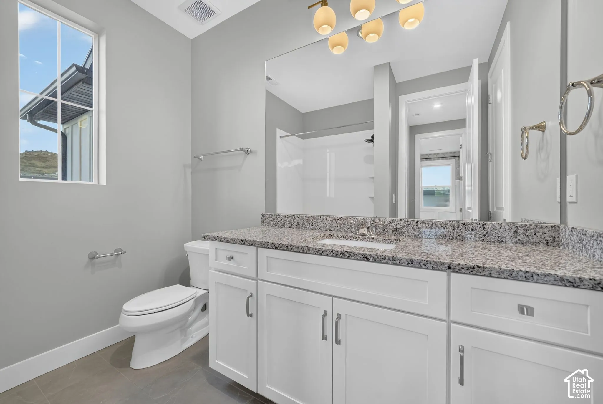 Bathroom featuring white shaker-style cabinetry, stone-surface countertop with an integrated basin, large-format mirror, multi-light fixture, and ceramic tile flooring