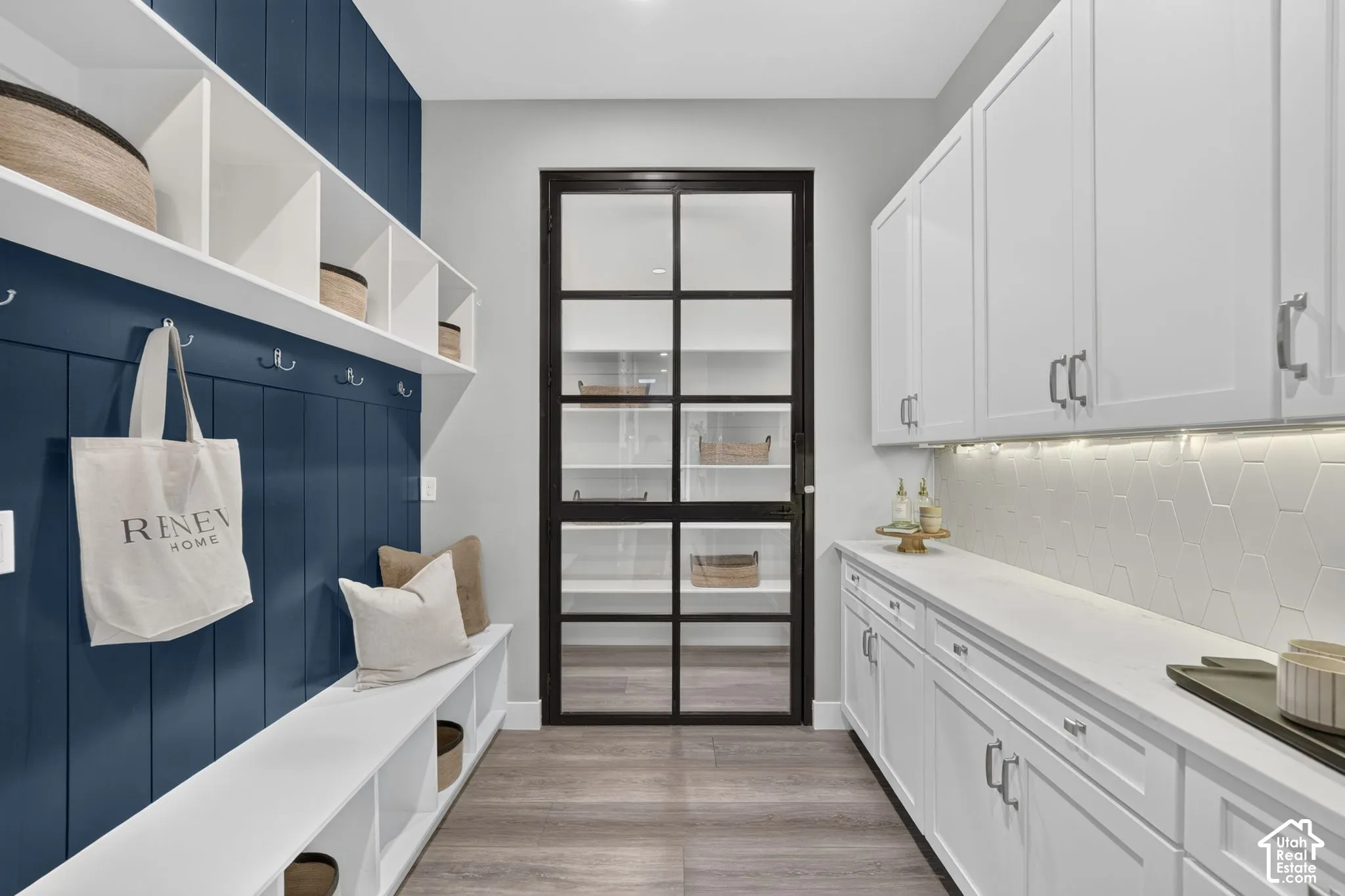 Custom built-in storage bench with vertical plank wall detailing, white cabinetry with countertop workspace, hexagonal tile backsplash, and a glass-paneled metal-frame door