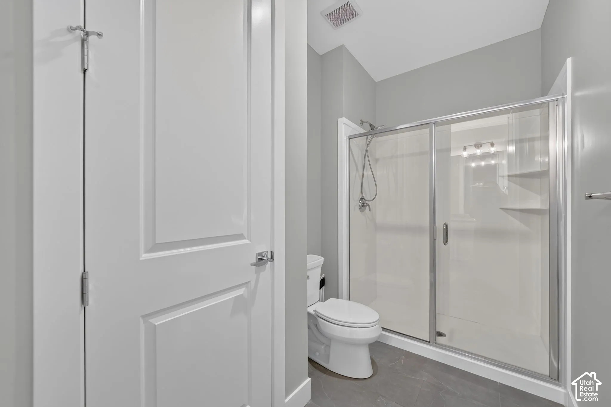 Bathroom featuring a glass-enclosed shower, integrated shelving, handheld shower fixture, and tiled flooring