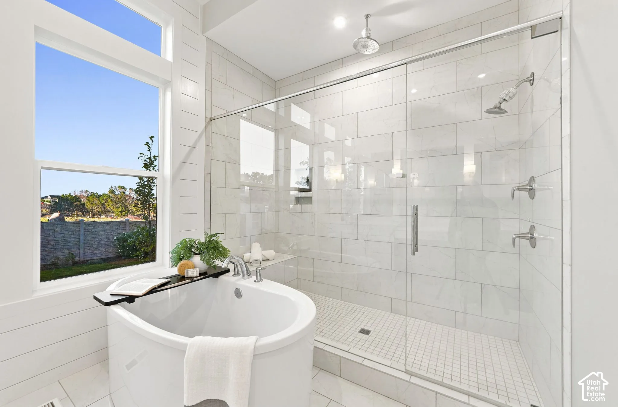 Freestanding oval soaking tub, glass-enclosed walk-in shower with floor-to-ceiling tile, dual shower heads including a ceiling-mounted rainfall fixture, and large transom window