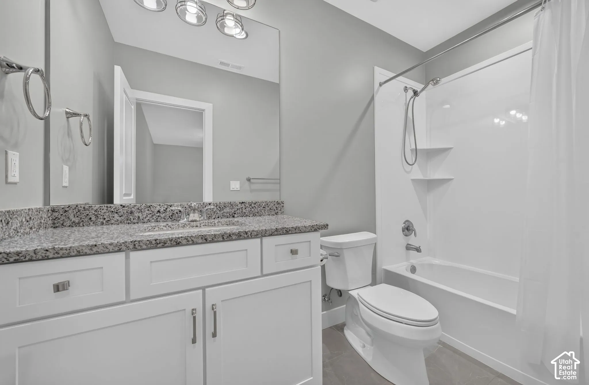 Bathroom featuring a white shaker-style vanity with stone-finish countertop, undermount sink, three-light fixture, and a tub-shower combination with built-in shelving