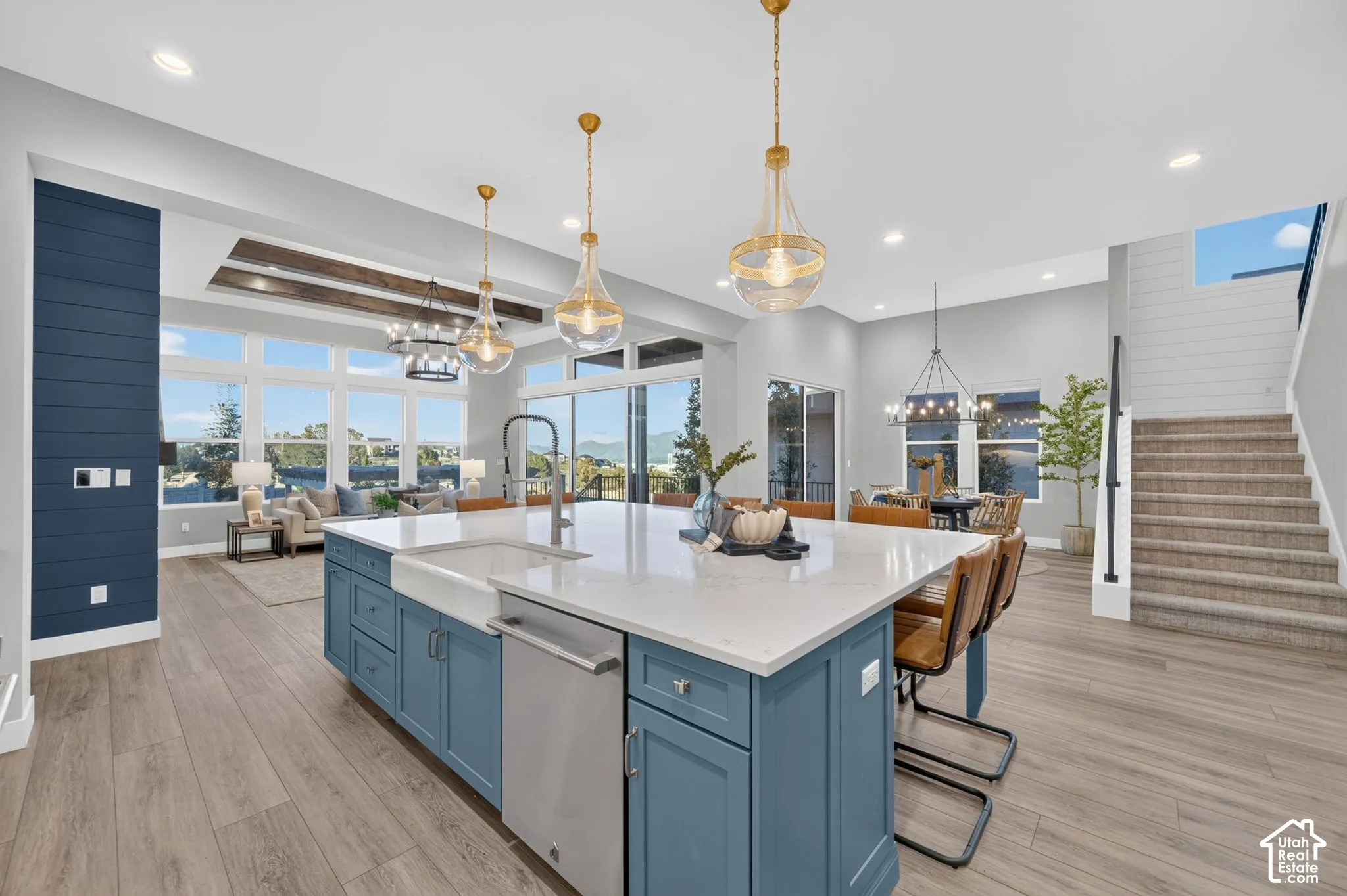 Kitchen featuring an oversized island with a farmhouse sink, quartz countertops, wood-finish flooring, decorative ceiling beams, and pendant lighting