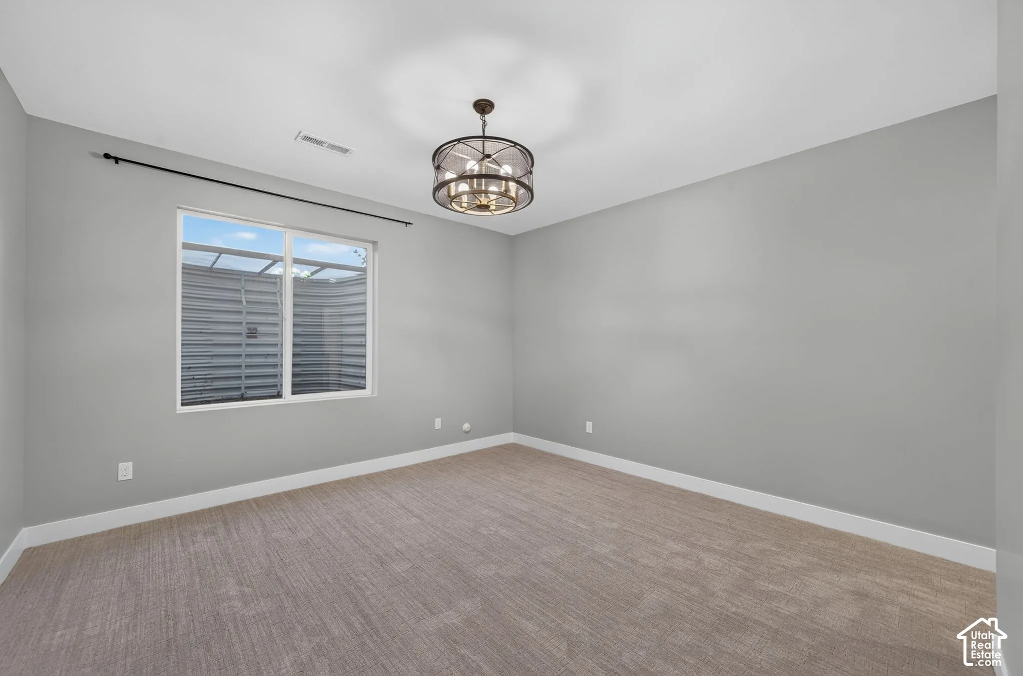 Room featuring neutral-toned carpeting, a drum-style chandelier with an oil-rubbed bronze finish, and a sliding window with a horizontal curtain rod