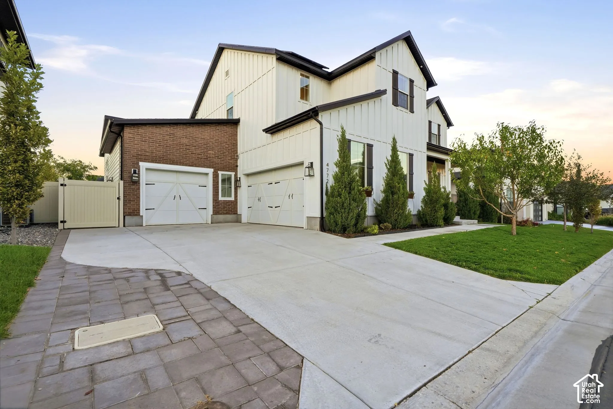 Two-story farmhouse-style exterior featuring vertical siding, brick masonry detailing, carriage-style garage doors, and a concrete driveway with paver accents