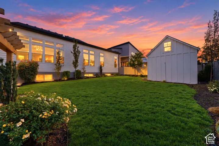 Expansive rear lawn featuring a wood-beam pergola, board-and-batten storage structure, and horizontal lap siding exterior