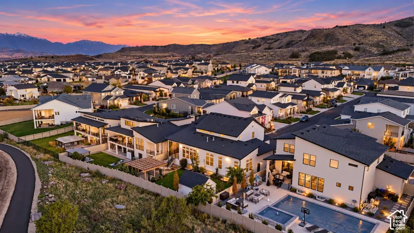 Aerial perspective featuring homes with varied rooflines and a mountain backdrop, showcasing private pools, covered patios, and manicured lawns